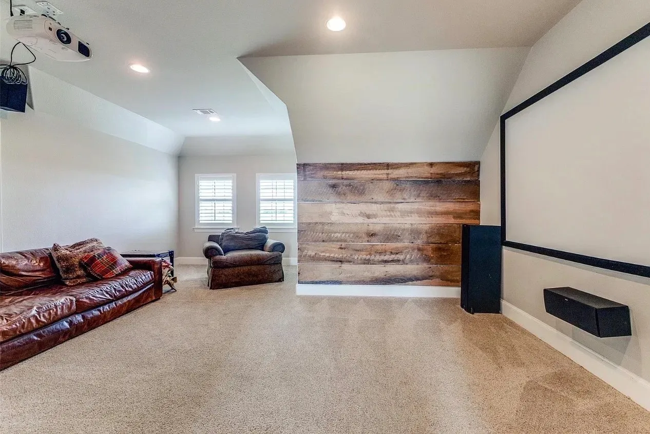 Media room featuring a mounted projector, wall-integrated screen, recessed lighting, wood-plank accent wall, and dual windows with shutters