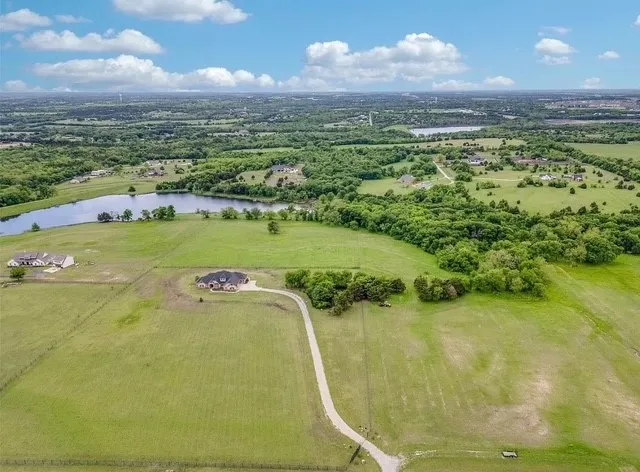 Aerial perspective of expansive acreage featuring mature tree lines, open pasture, a winding concrete driveway, and direct frontage on a private lake