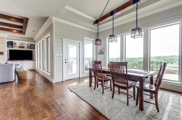Tray ceiling with exposed wooden beams, plank wall paneling, built-in cabinetry, wood-finish flooring, and industrial-style pendant lighting