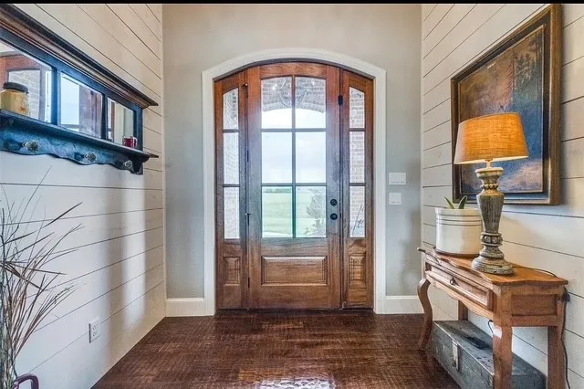 Entryway featuring an arched, six-panel wood-framed glass door with matching sidelights, horizontal white plank wall paneling, and dark wood-finish flooring