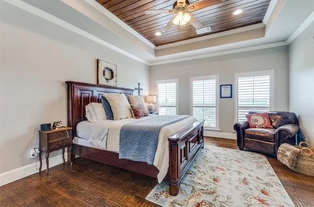 Tray ceiling with wood-finish paneling, recessed lighting, central ceiling fan, and three windows with louvered shutters