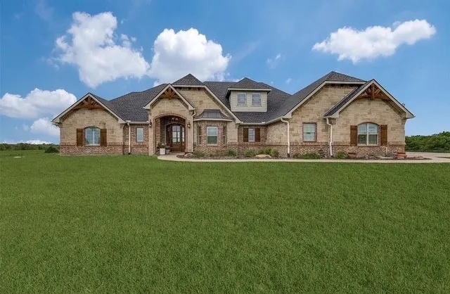 Single-story residence featuring stone and brick masonry, arched entryway, timber gable accents, and a multi-pitch roofline