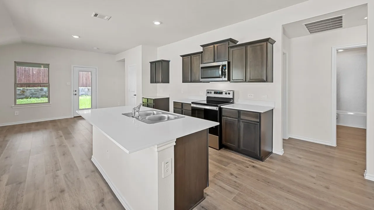 Kitchen island with dual basin sink, white countertops, wood-finish flooring, dark wood cabinetry, and stainless steel appliances