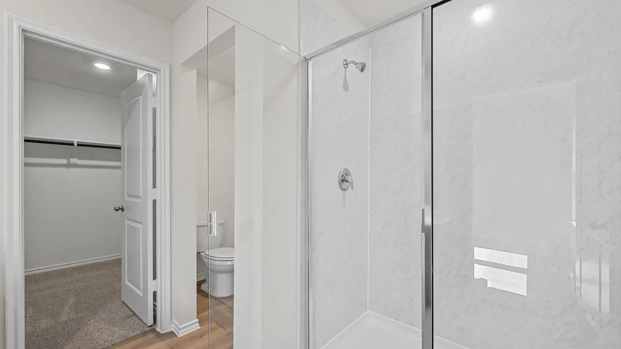 Glass-enclosed shower with a chrome showerhead, white shower surround, and matching chrome fixtures