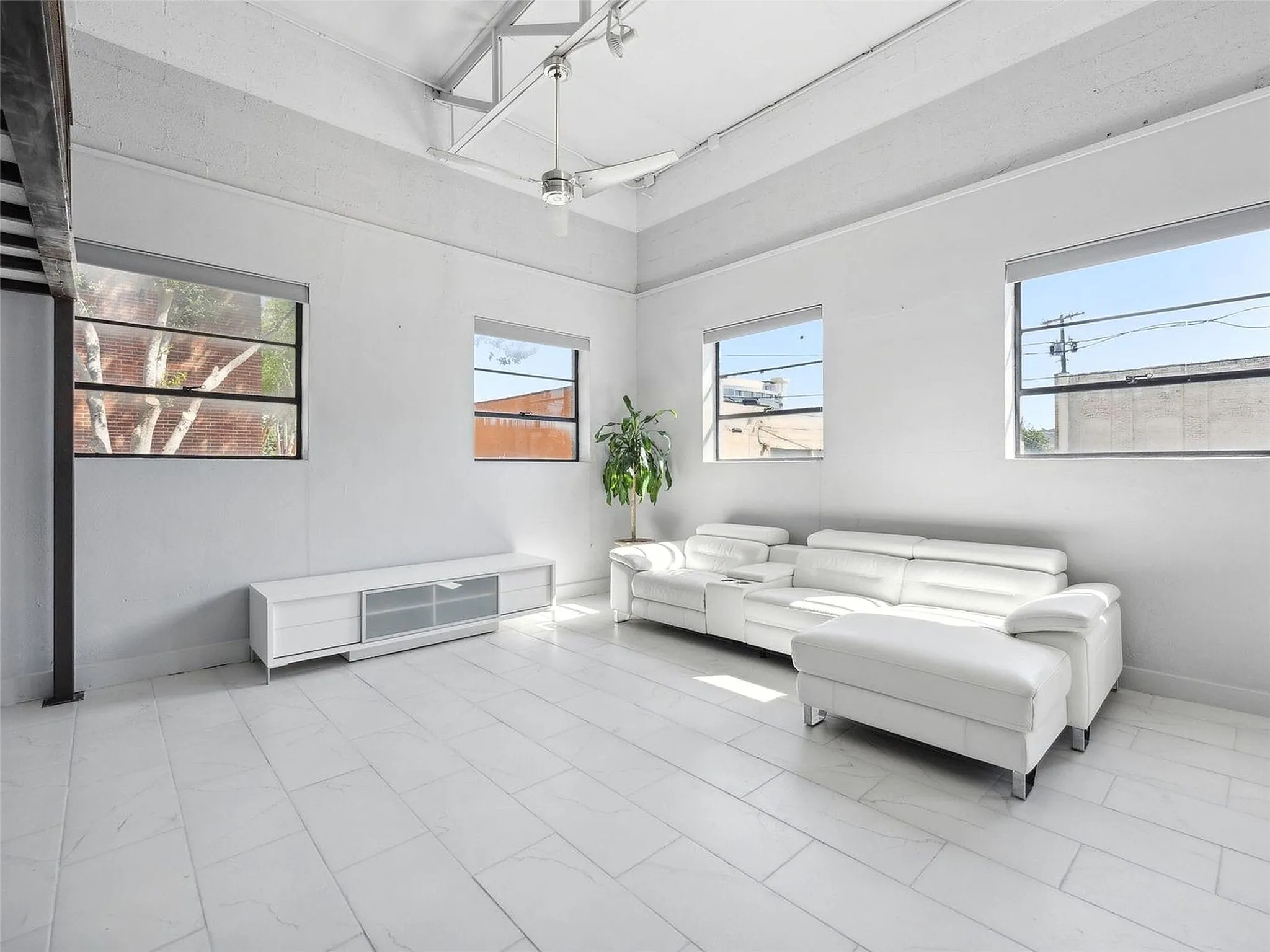 High ceilings with exposed industrial truss, large multi-pane windows, and light-toned tile flooring
