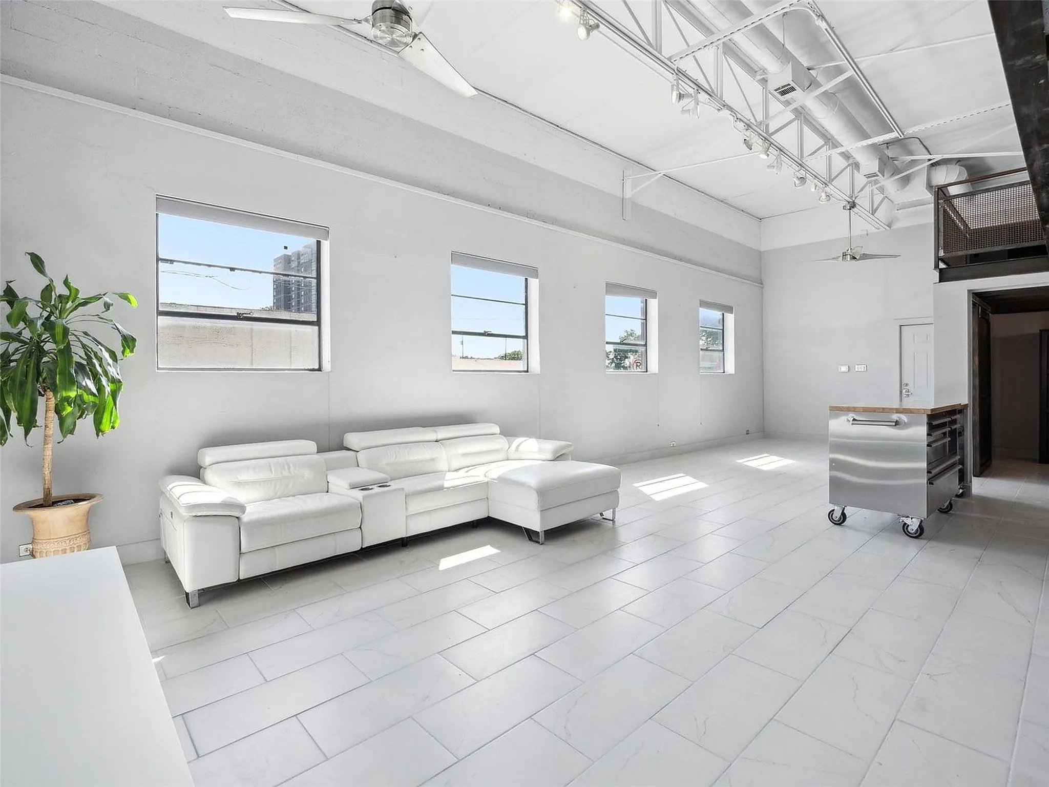 Industrial-style interior featuring high ceilings with exposed trusses, large-format tile flooring, oversized windows, and overhead track lighting