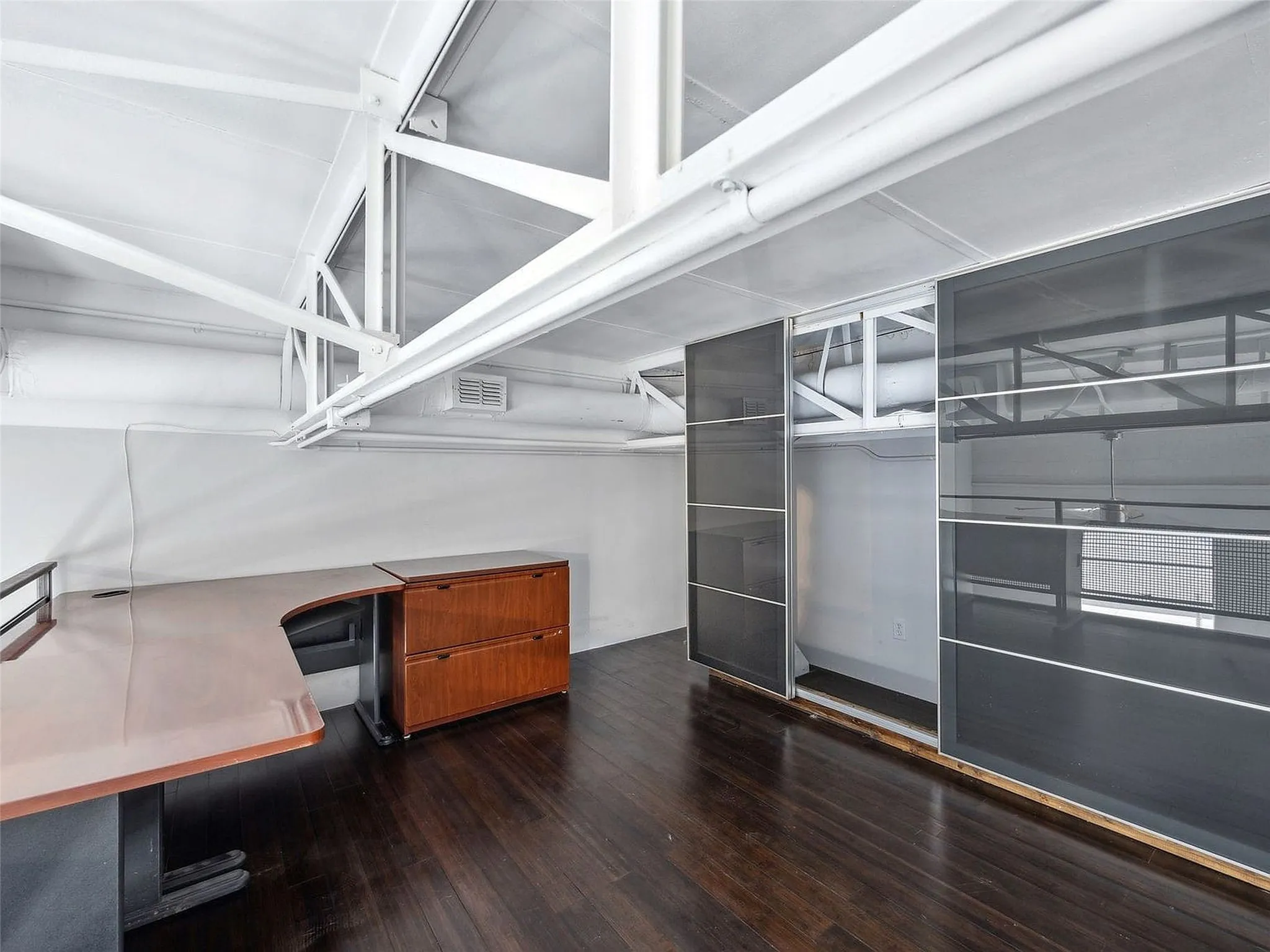 Industrial-style interior featuring exposed white structural steel trusses, dark wood-finish flooring, and floor-to-ceiling sliding glass storage panels with metal frames