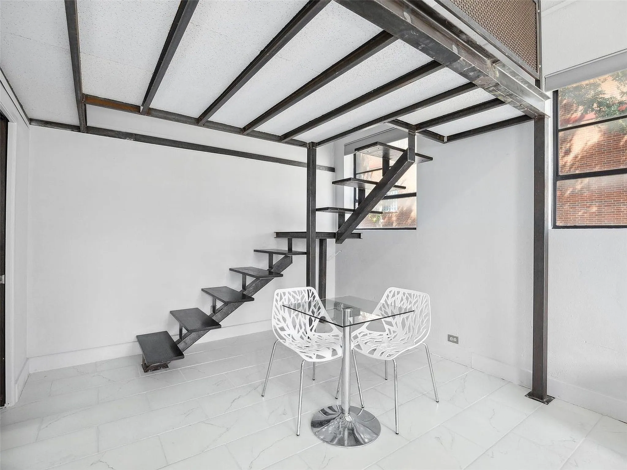 Industrial-style metal mezzanine structure featuring exposed steel beams, custom-welded staircase with floating treads, large multi-pane windows, and white tile flooring