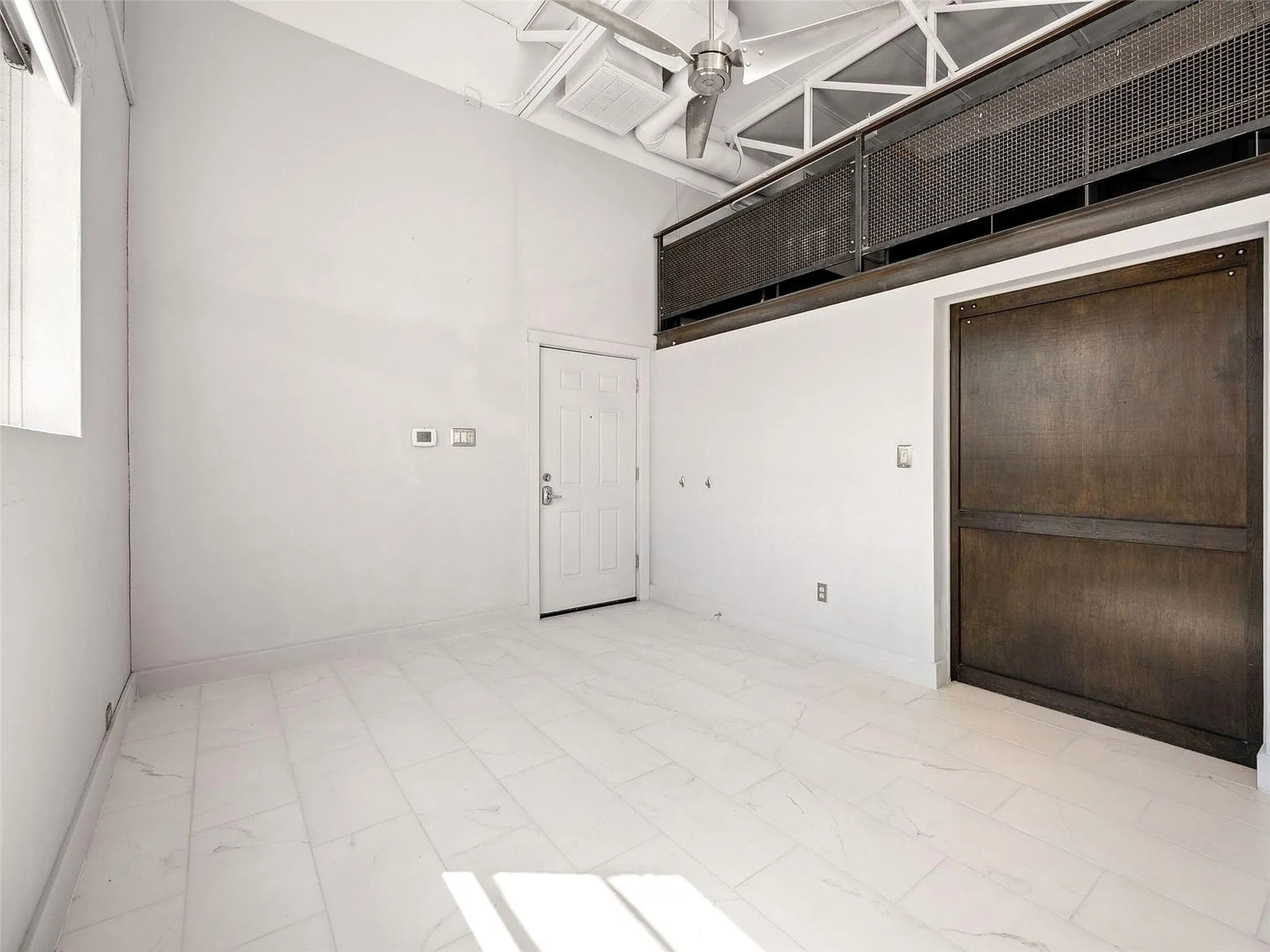 High ceilings featuring exposed industrial-style trusses and a ceiling fan, large dark-finish sliding door, and neutral tile flooring