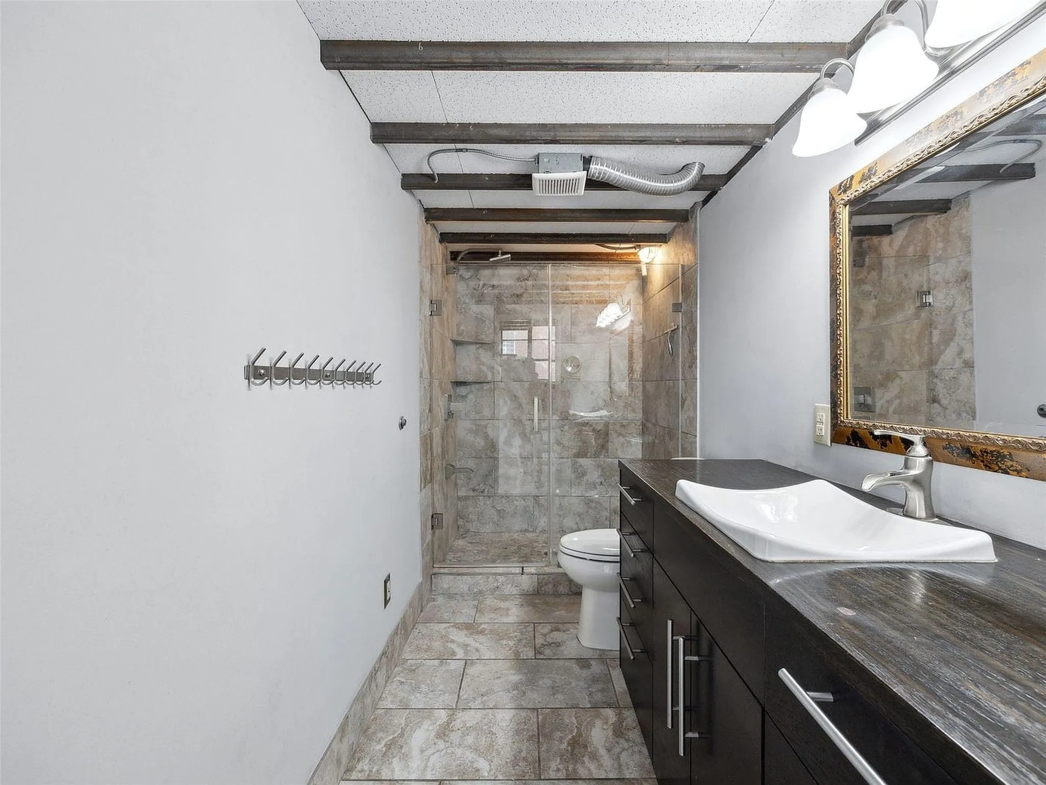 Bathroom featuring an integrated vanity with a rectangular vessel sink, stone-surface countertop, exposed ceiling beams, and a walk-in shower with tile surround and glass enclosure