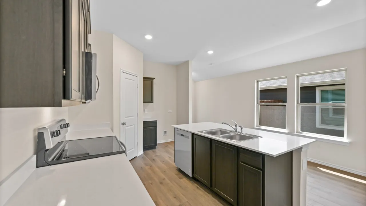 Kitchen featuring an island with double basin sink, quartz countertops, wood-finish flooring, dark wood cabinetry, and recessed lighting