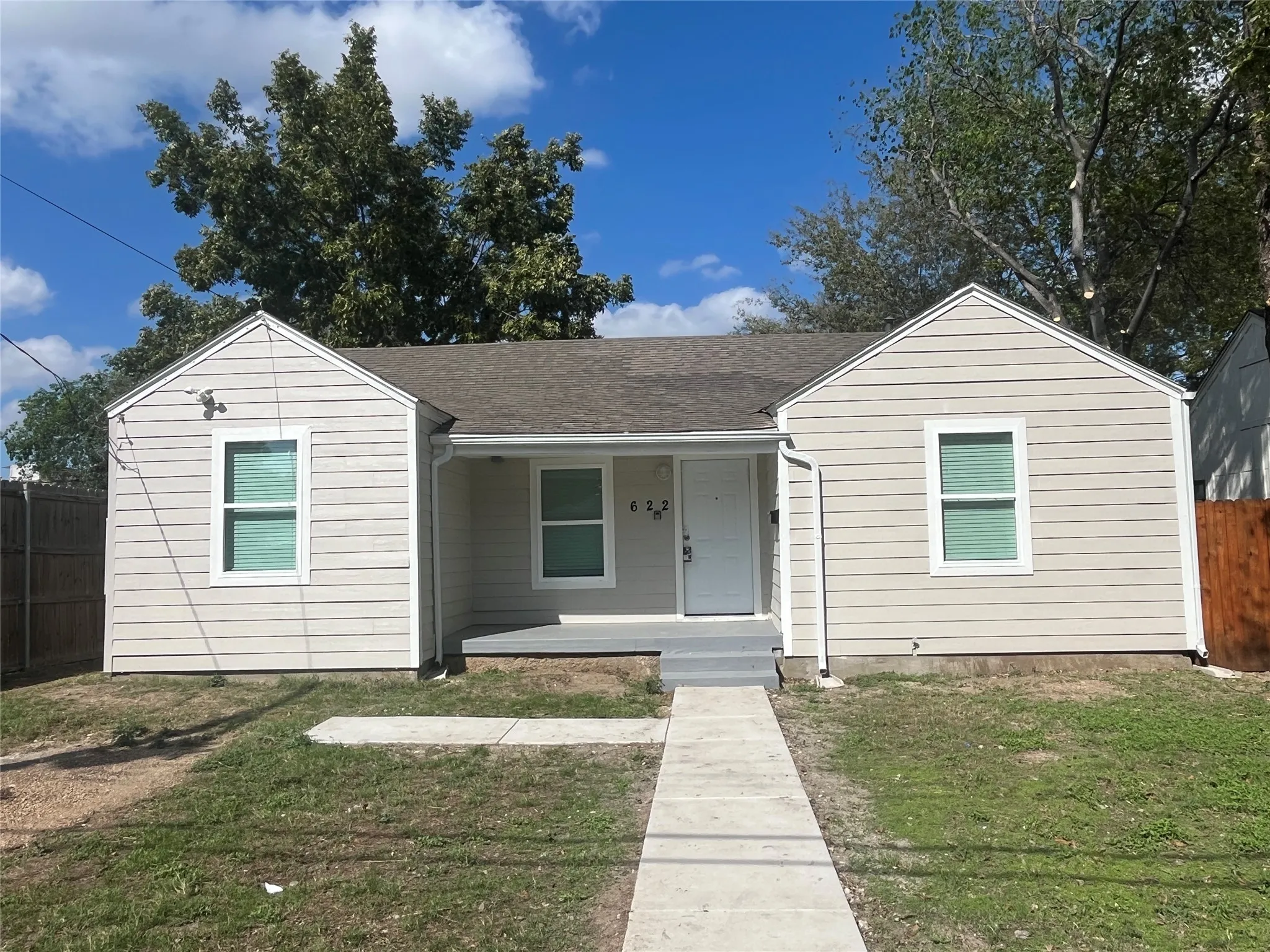 Single-story exterior featuring light-toned horizontal siding, double-gable roofline, recessed front entry, and concrete walkway