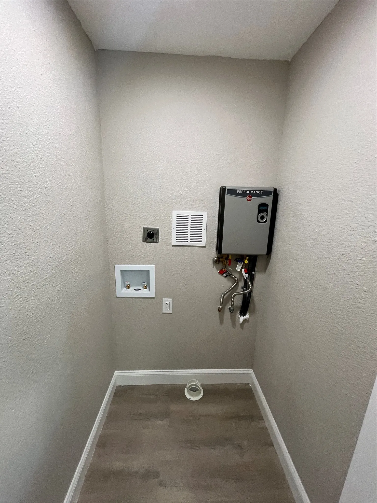 Dedicated utility area featuring wood-finish flooring, a wall-mounted tankless water heating unit, and integrated plumbing hookups