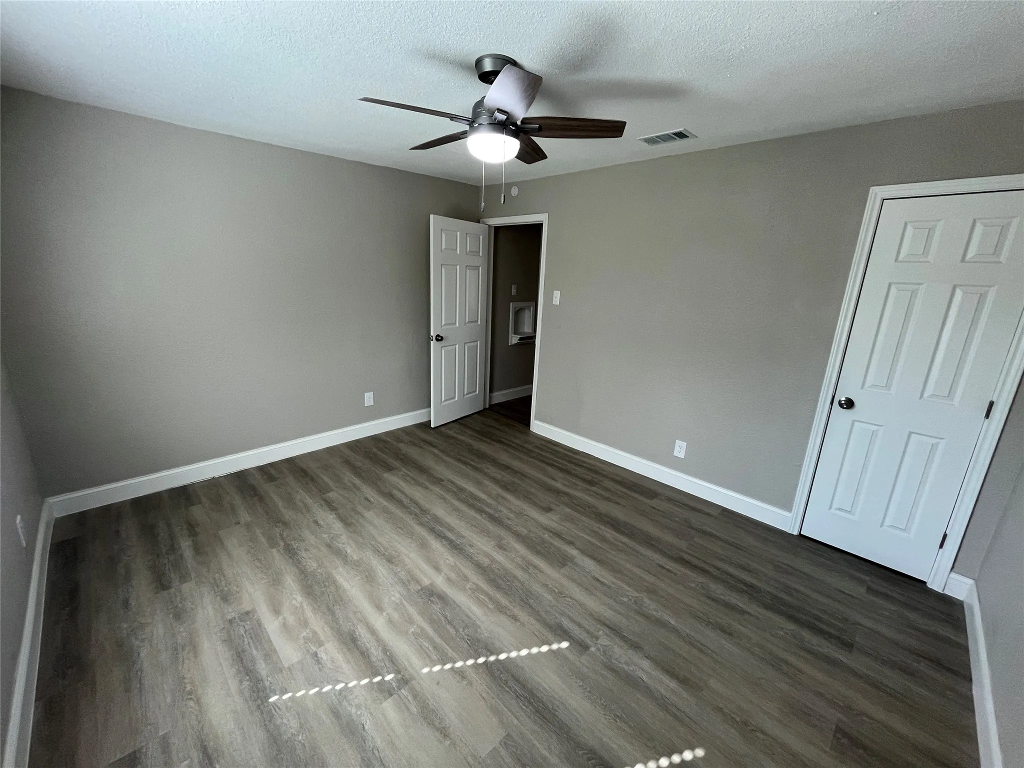 Room featuring wood-finish flooring, neutral wall paint, a ceiling fan with integrated lighting, and two six-panel interior doors
