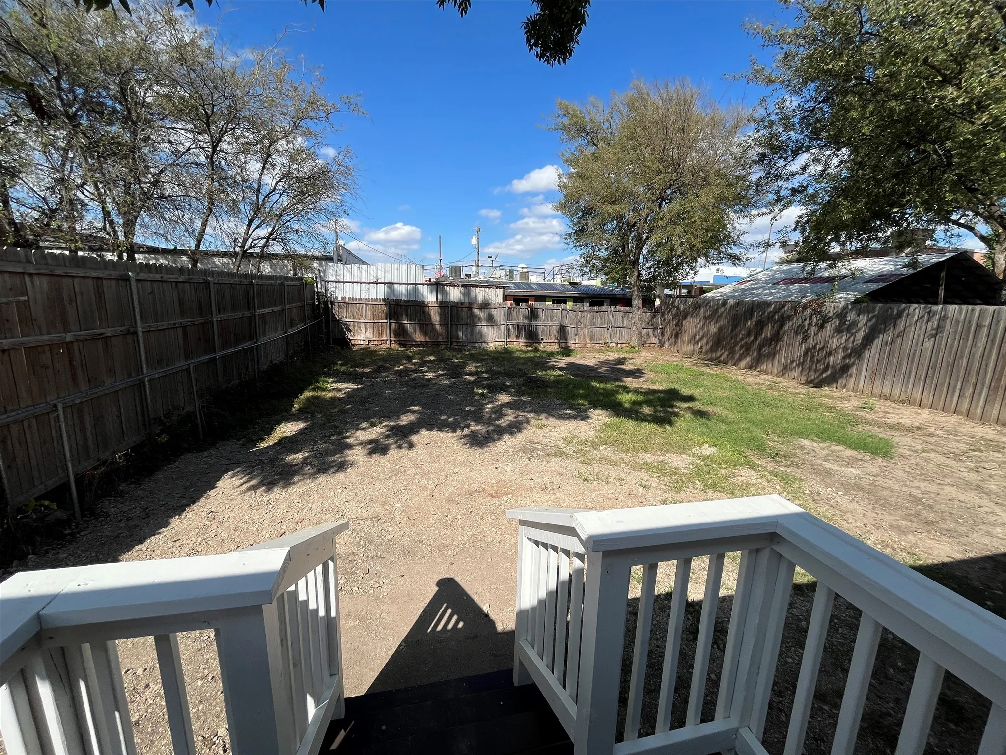 Backyard area enclosed by a wooden privacy fence, featuring a white-railed elevated deck and mature trees