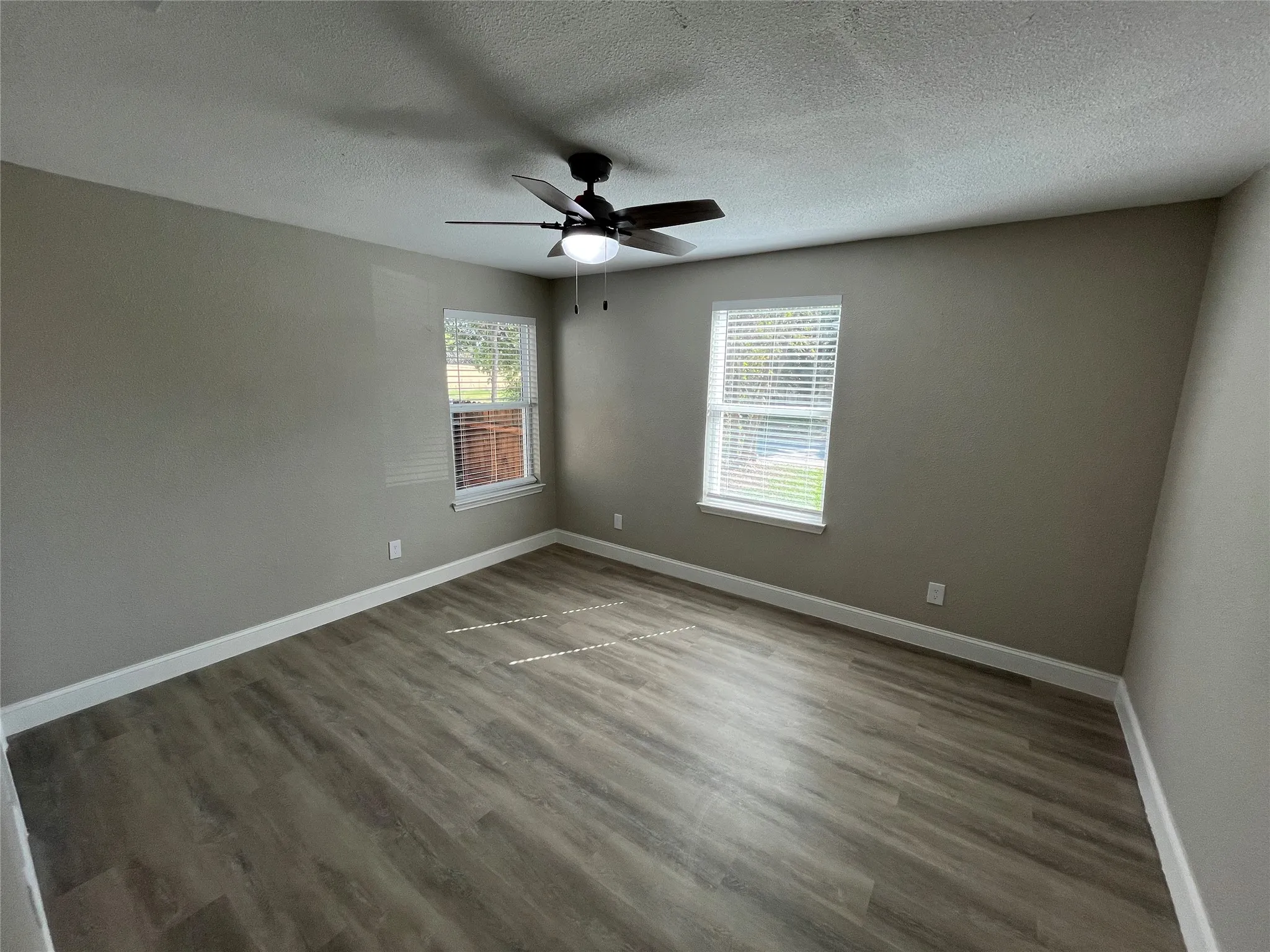 Room featuring wood-finish flooring, dual windows with blinds, and a central ceiling fan with integrated lighting