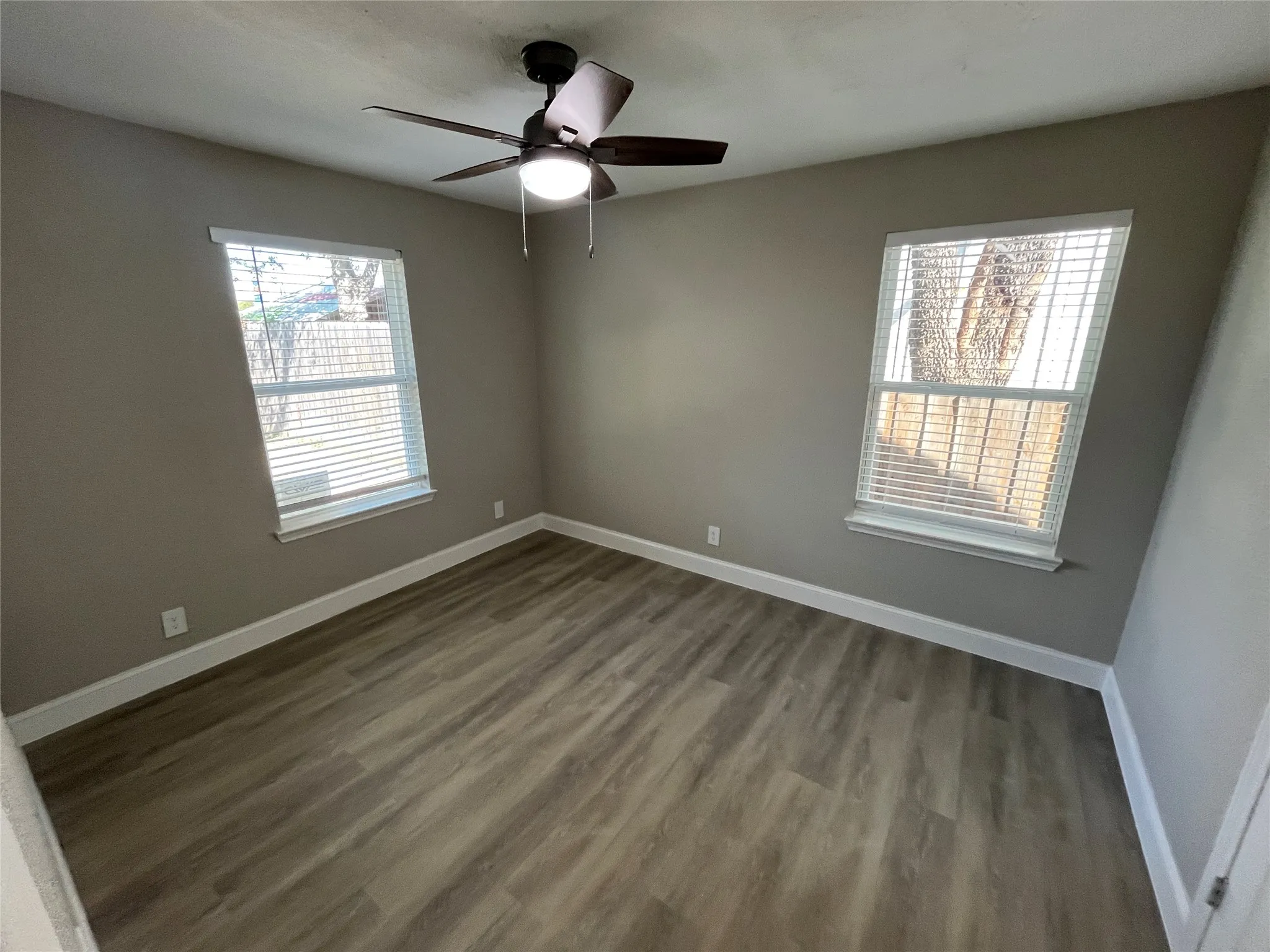 Neutral-toned walls paired with wood-finish flooring, dual windows, and a ceiling-mounted light fixture with a fan