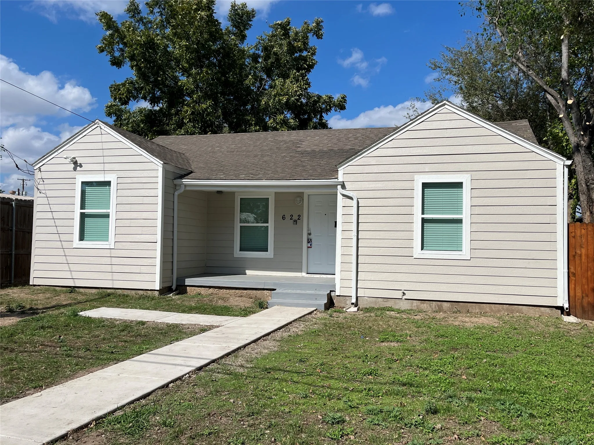 Single-story exterior featuring light-toned horizontal siding, a covered front entry porch, a concrete walkway, and a roof with composite shingles