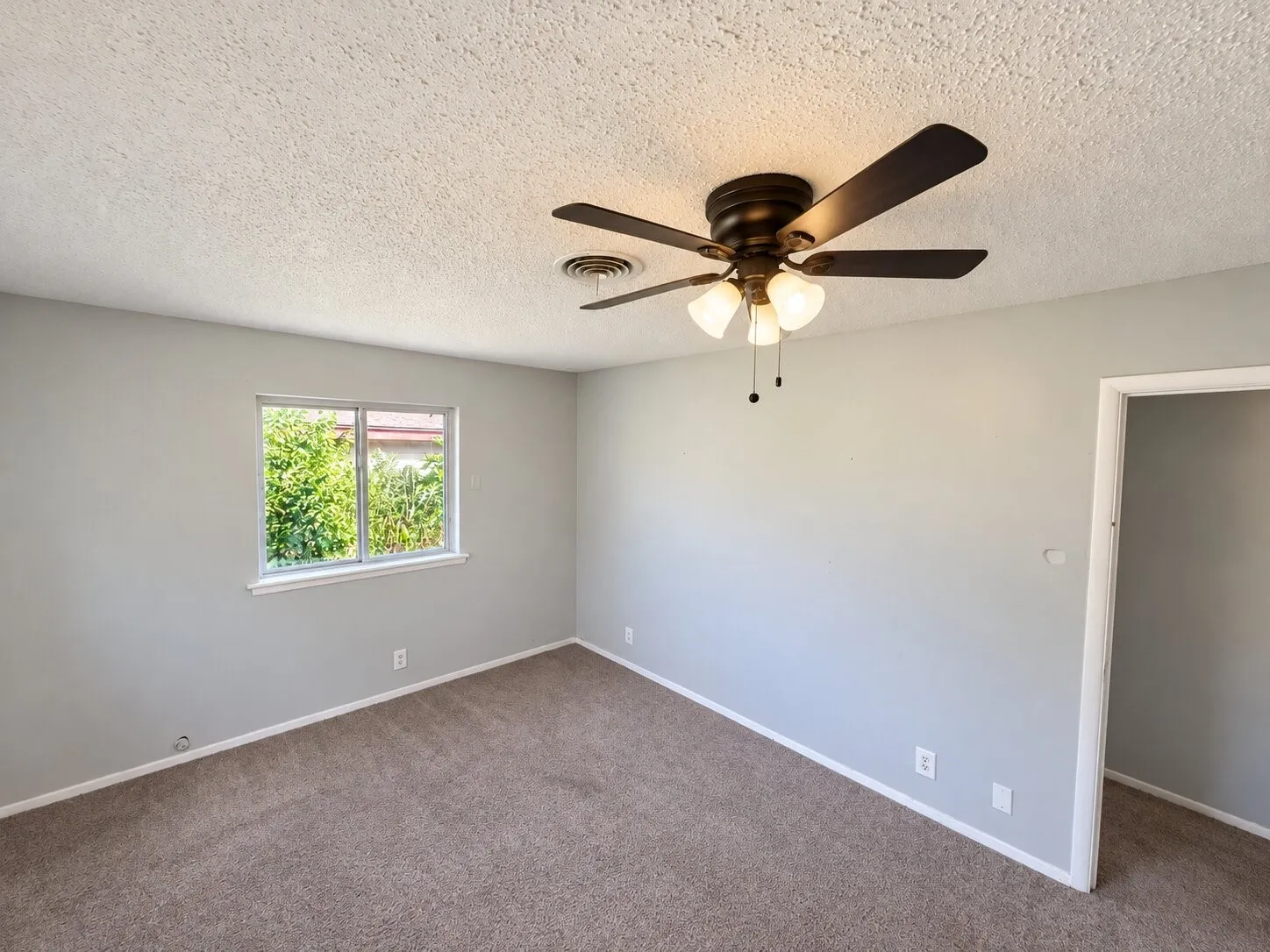 Neutral-toned interior featuring wall-to-wall carpeting, a multi-pane sliding window, and a dark-finish ceiling fan with integrated glass-shade lighting