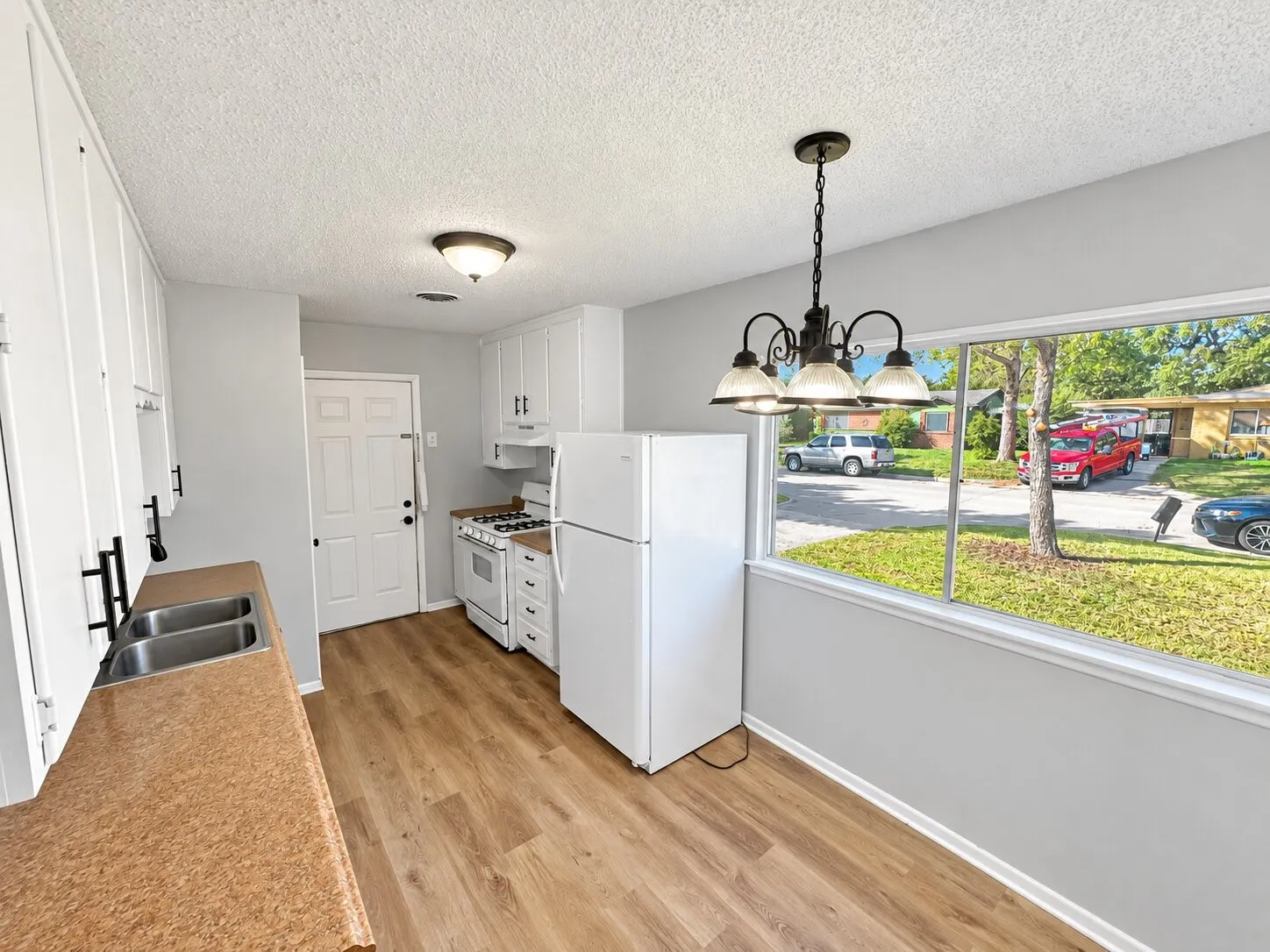 Kitchen featuring white shaker-style cabinetry, matte black hardware, wood-finish flooring, dual-basin stainless steel sink, and a large picture window