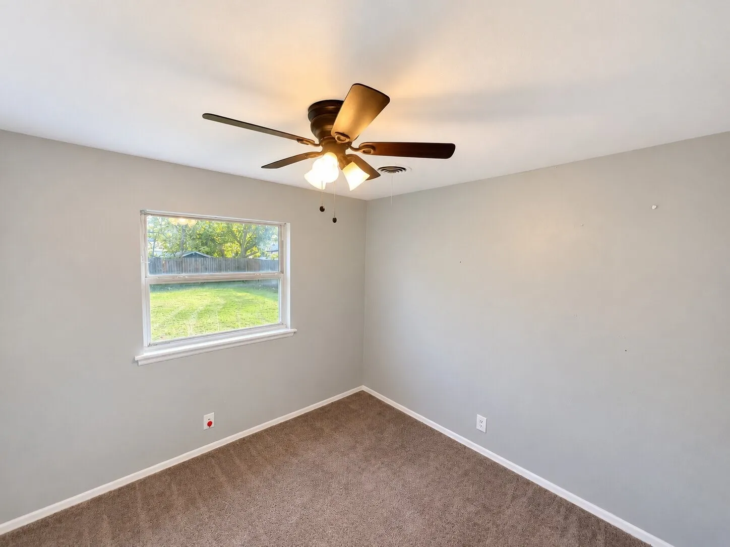 Neutral-toned interior space featuring carpeting, a single-hung window, and a ceiling-mounted light fixture with a central fan