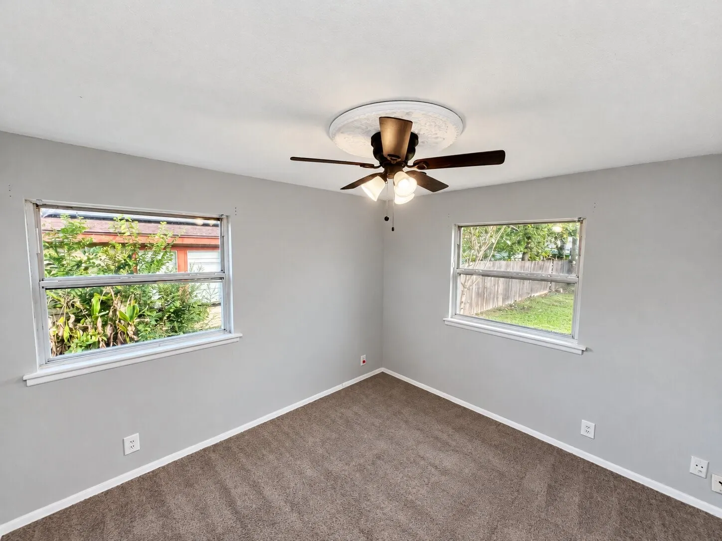 Neutral-toned interior featuring dual windows, carpeting, and a central ceiling fan with a light fixture and decorative medallion