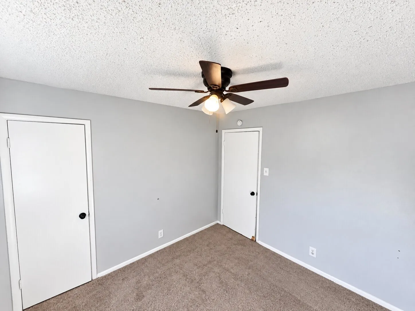 Neutral-toned interior walls, textured ceiling, carpeted flooring, two interior doors, and a ceiling-mounted light fixture with a three-blade fan