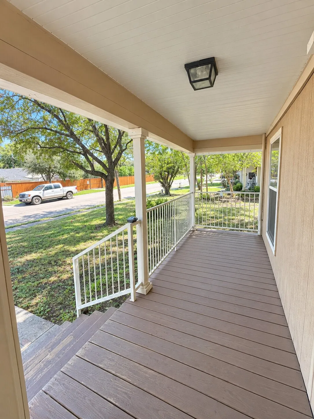 Covered front porch featuring wood-finish decking, white railings, and a flush-mount outdoor light fixture