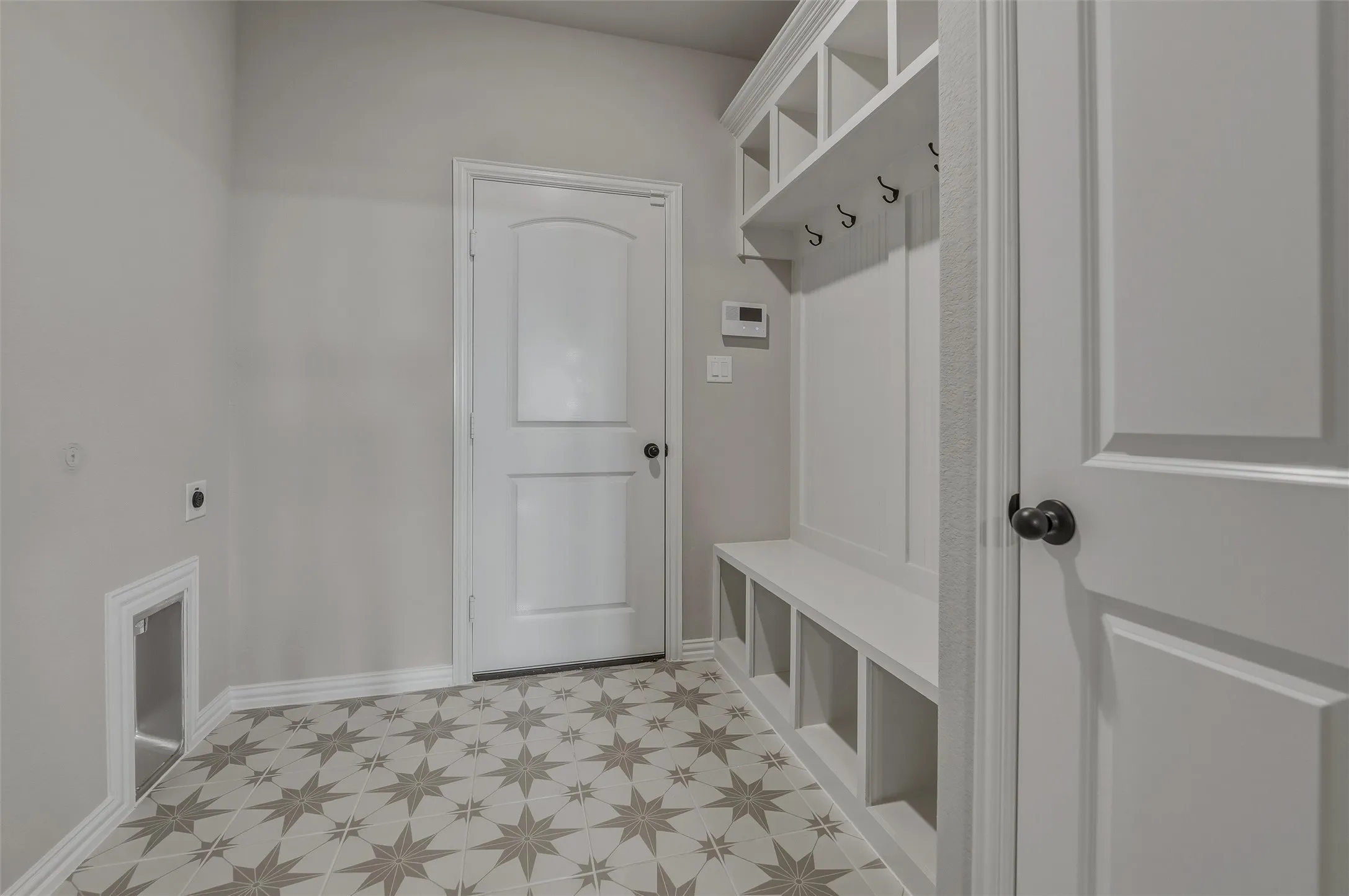 Mudroom featuring patterned floor tiles, built-in bench with storage cubbies, and overhead shelving with hooks