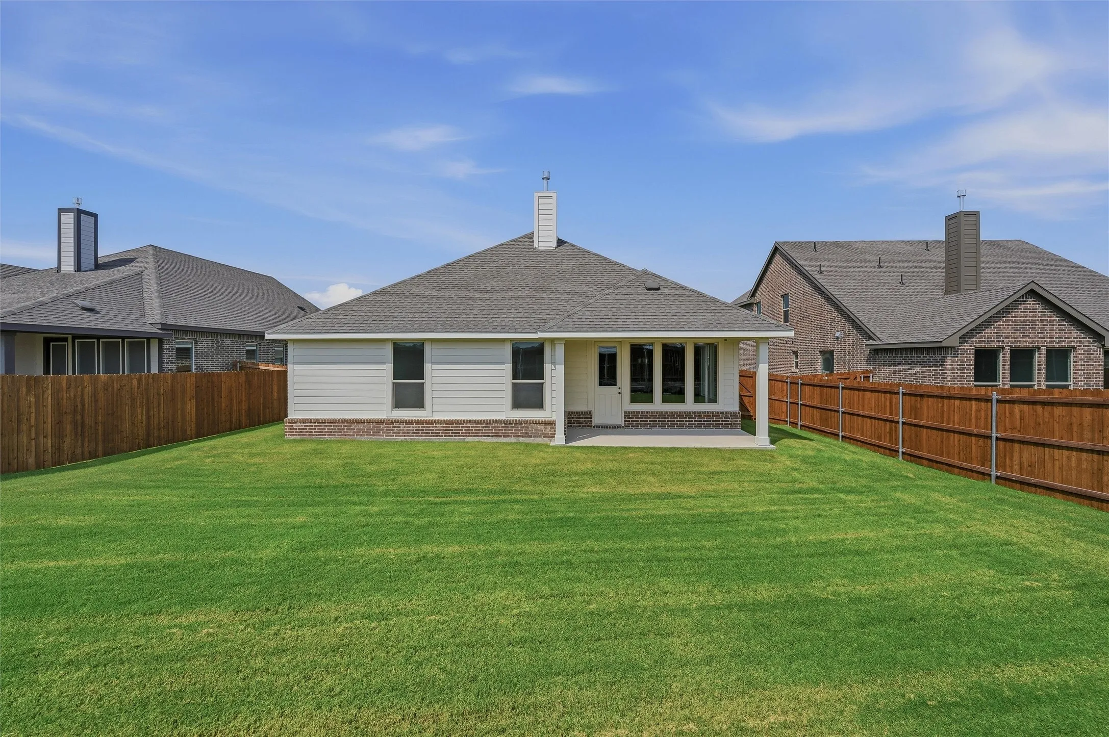 Expansive backyard featuring a manicured lawn, wood fencing, and a covered patio with columns