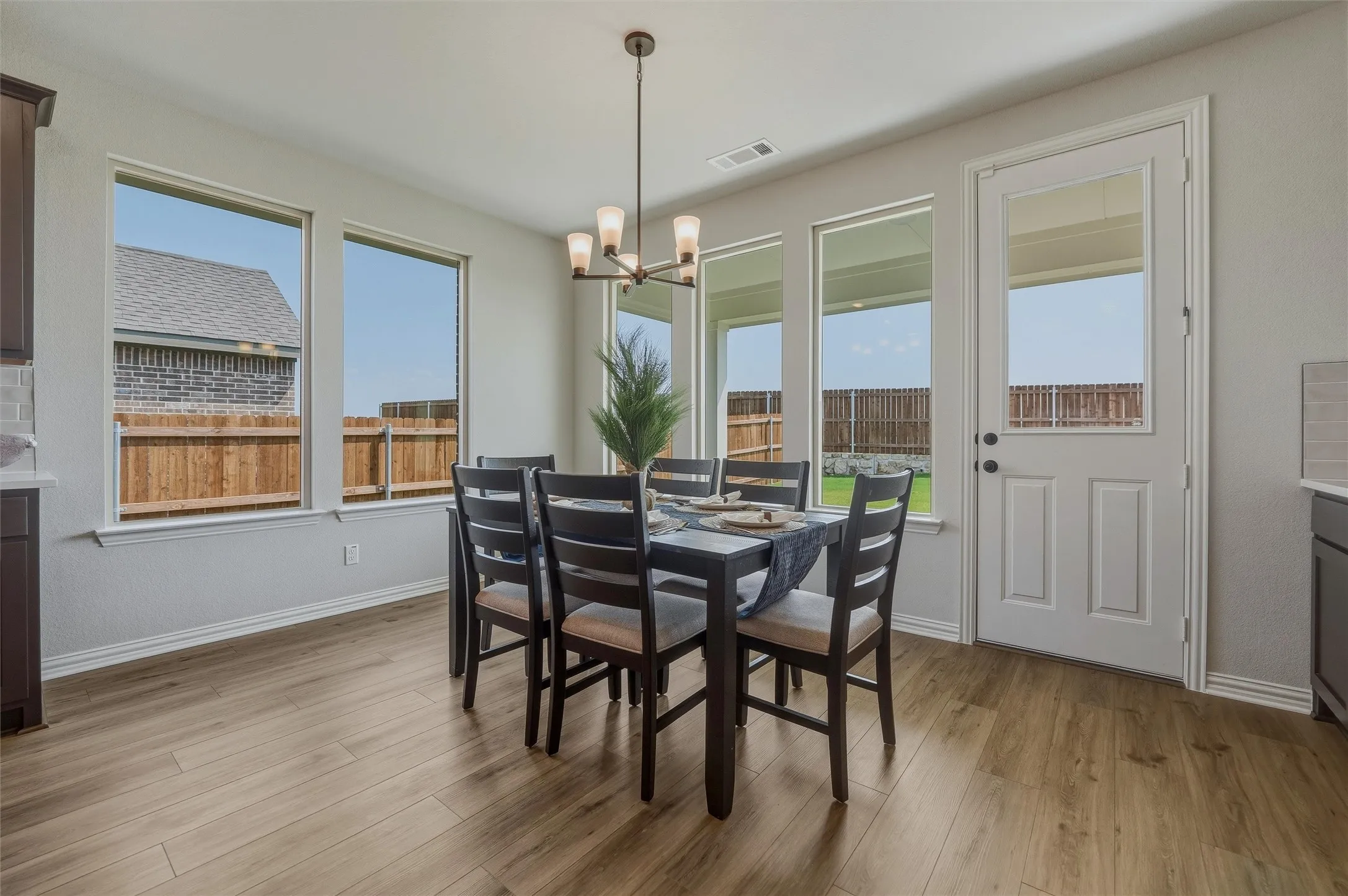 Wood-finish flooring, multiple large windows, a built-in ceiling light fixture, and a white door with an upper glass panel