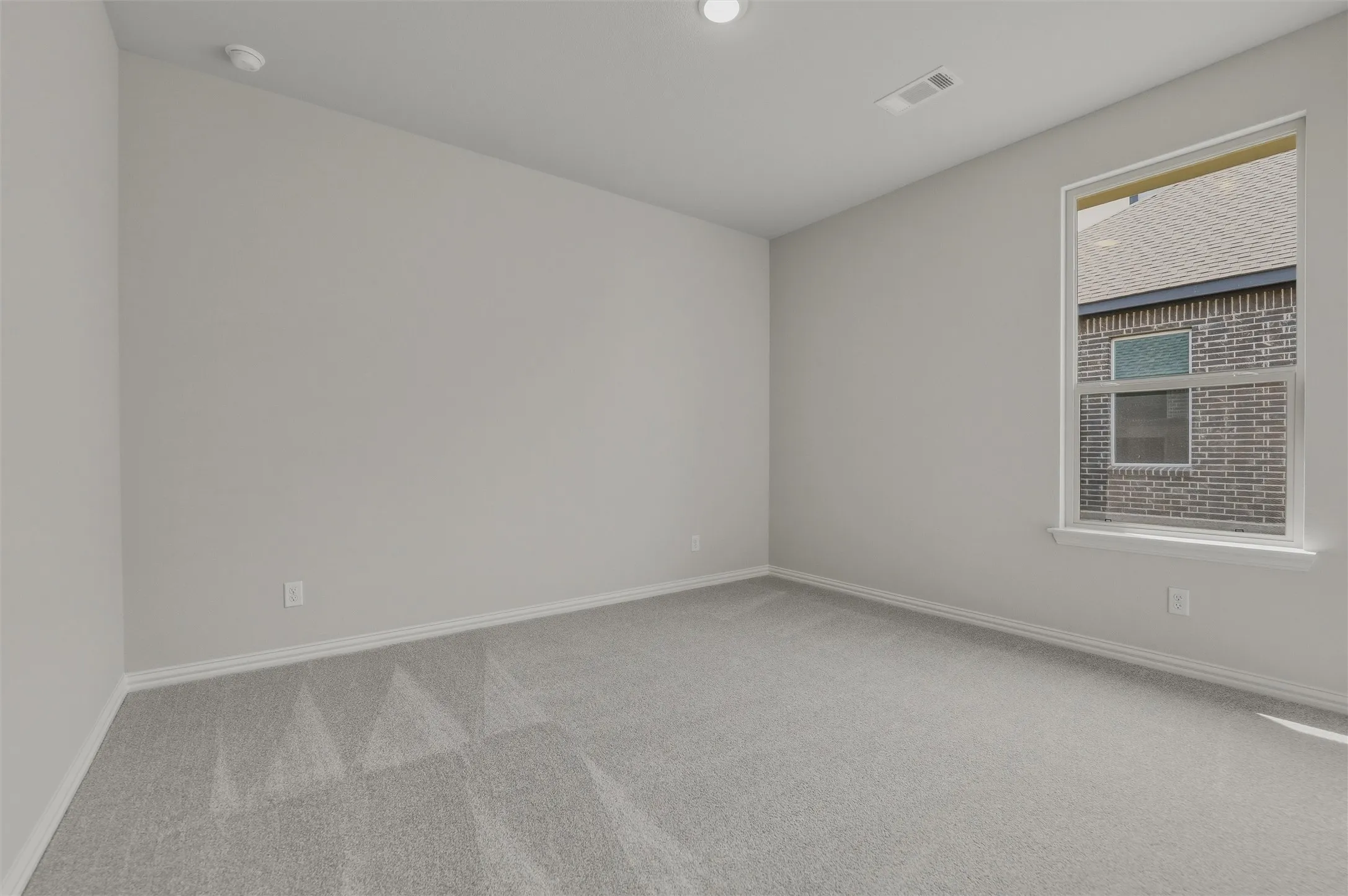 Bright secondary bedroom featuring neutral wall finishes, recessed ceiling lighting, carpet flooring, and a large window with natural light and brick exterior views