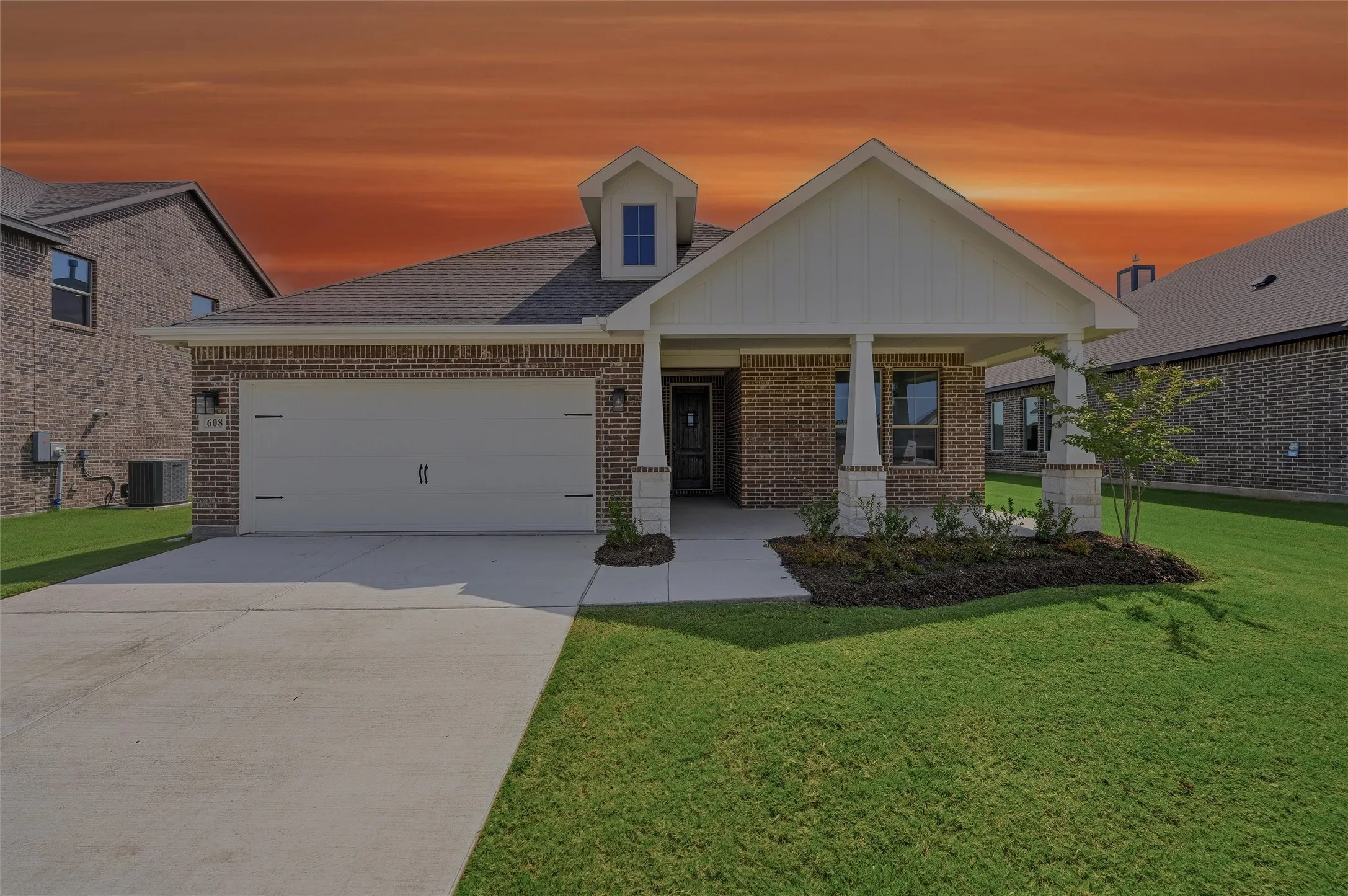 Brick exterior with a covered porch entry, dormer accent, attached garage, and concrete driveway