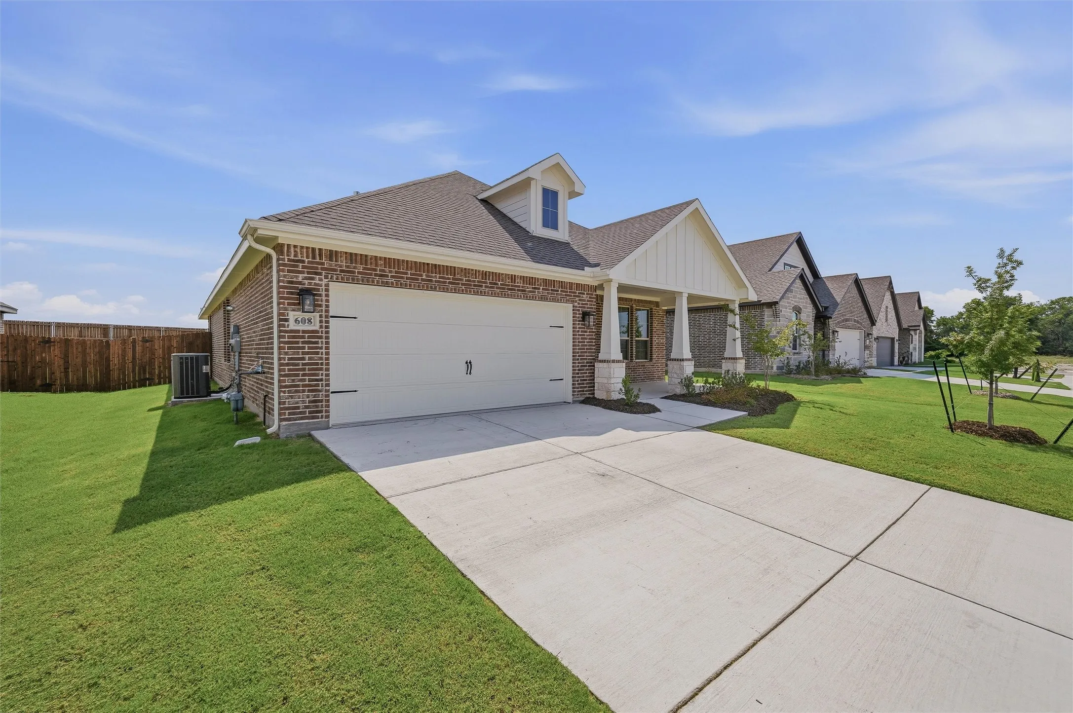 Brick exterior with white trim accents, attached two-car garage, covered entry porch, concrete driveway, and manicured lawn