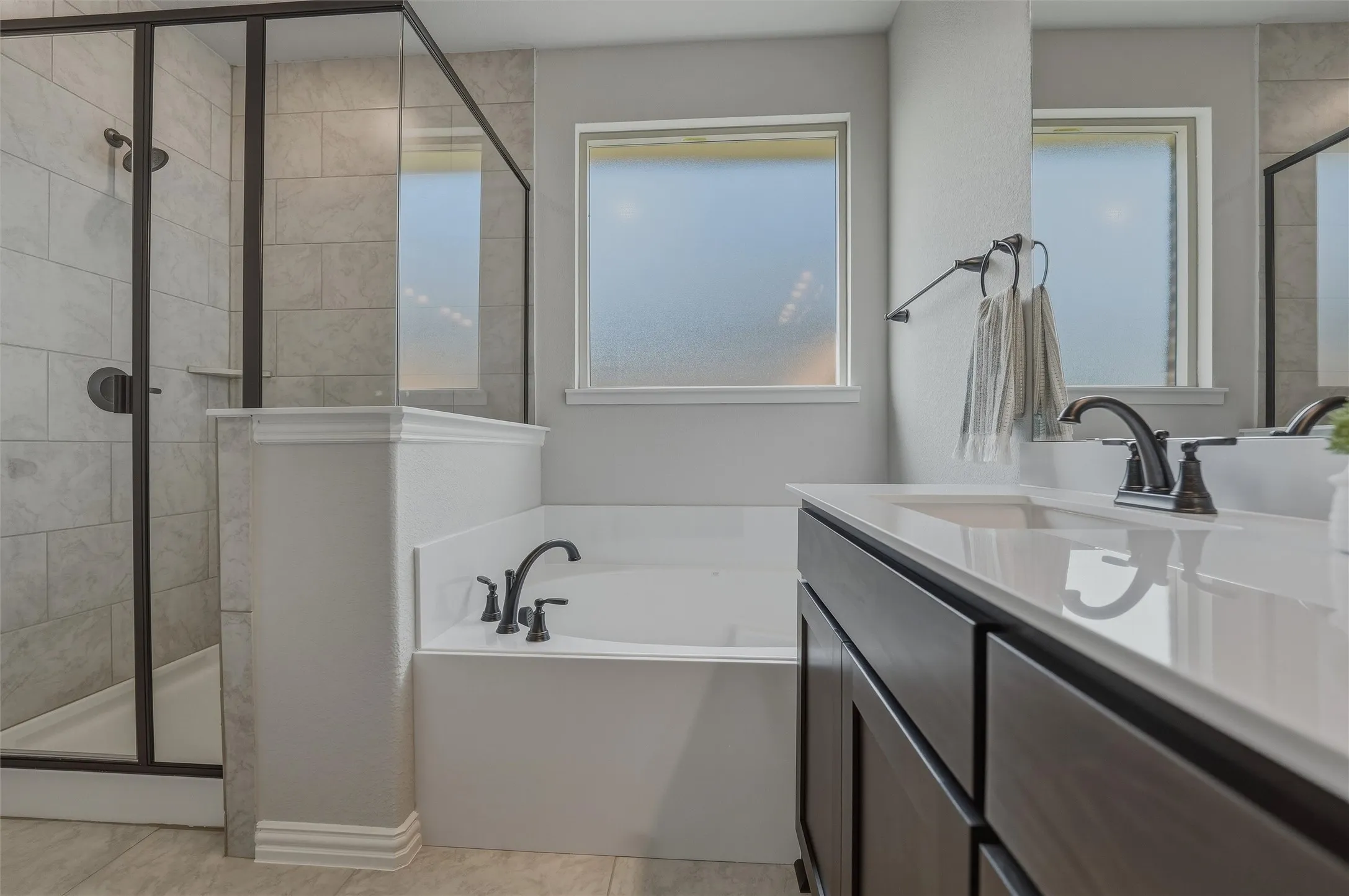 Built-in soaking tub, separate glass-enclosed shower with tile surround, dark wood-finish vanity with an integrated sink, and dual frosted windows