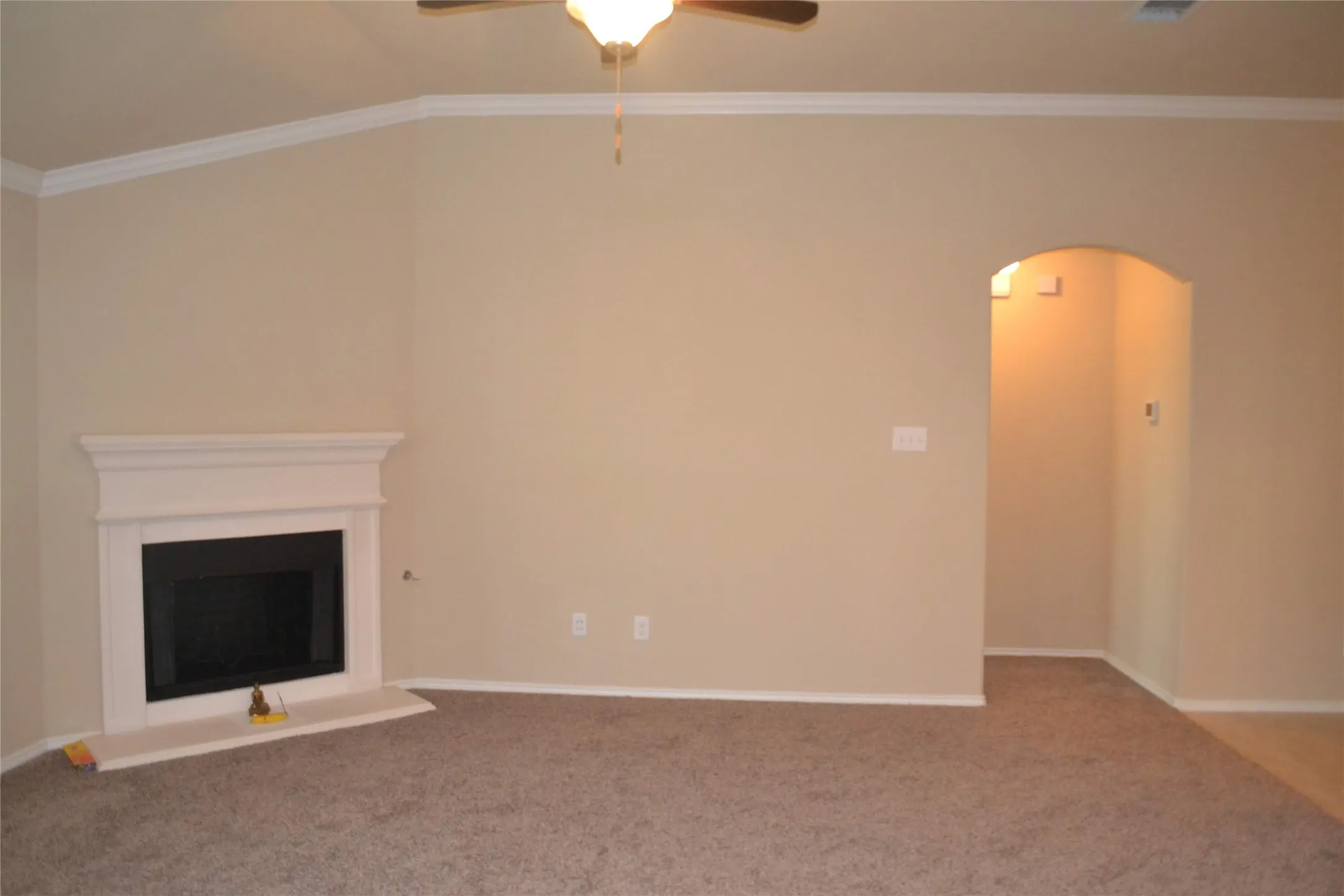 Vaulted ceiling with a central ceiling fan, fireplace featuring a white mantle and surround, and an arched entryway