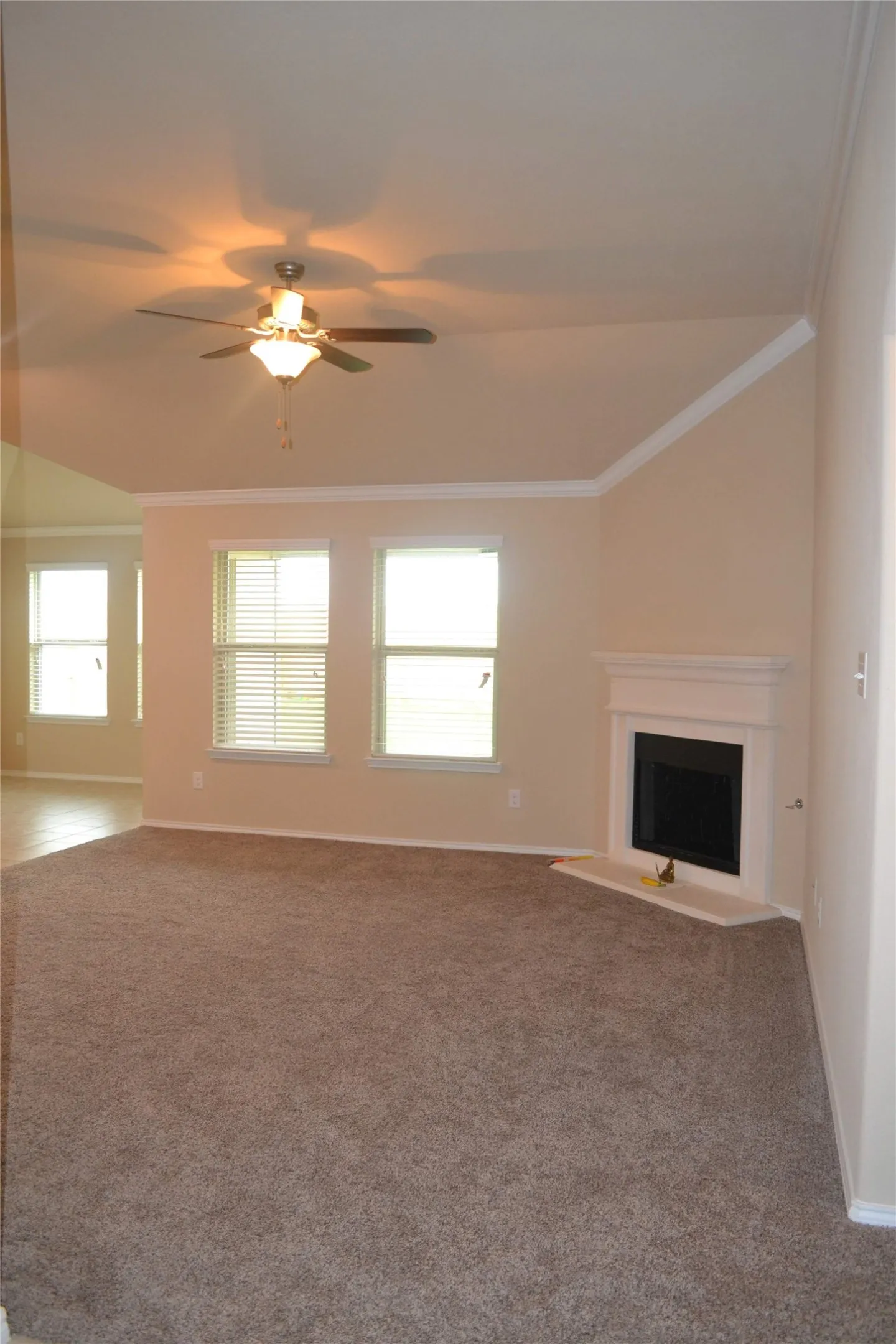 Vaulted ceiling featuring a central lighted ceiling fan, neutral carpeting, and a fireplace with a white mantel and stone-finish hearth