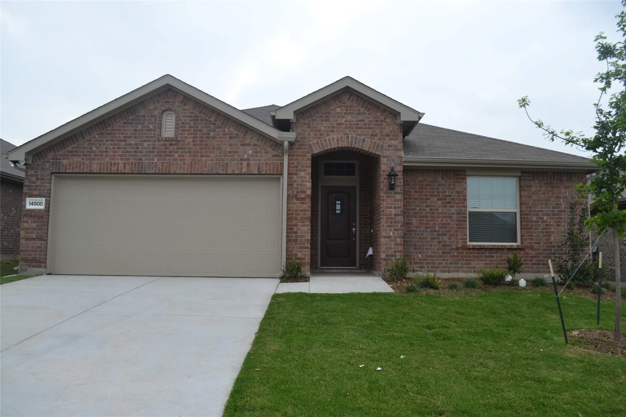 Single-story brick exterior featuring a covered entryway with a brick archway, a double-gabled roofline, and a concrete driveway leading to a two-car garage
