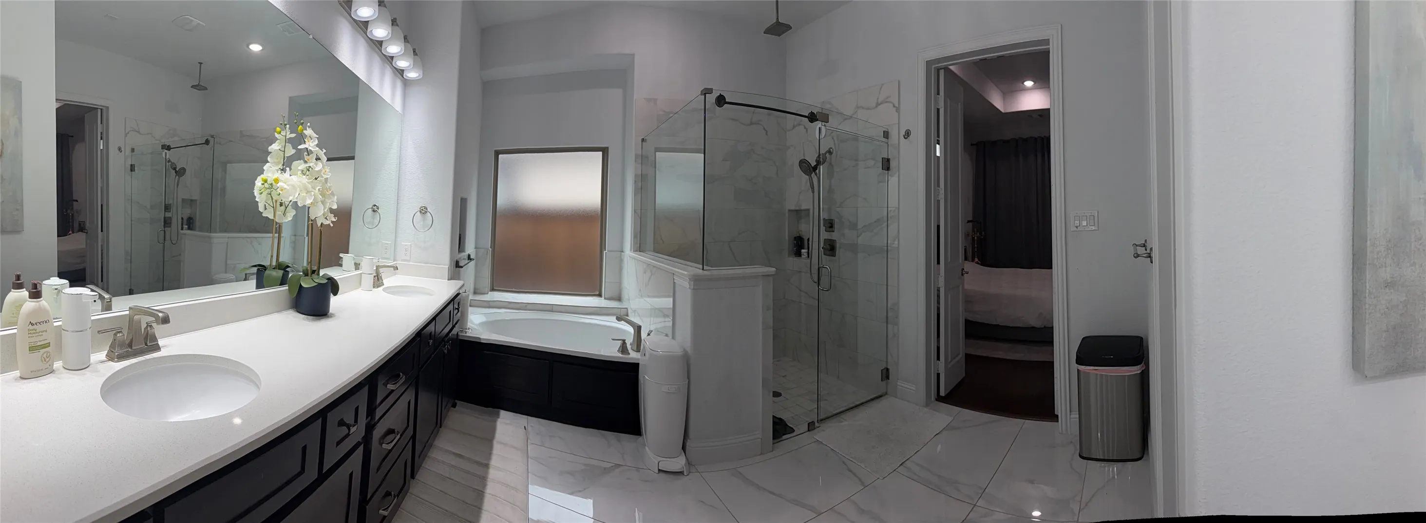 Double vanity with a composite countertop, expansive wall-to-wall mirror, built-in soaking tub, and a glass-enclosed shower with tiled surround