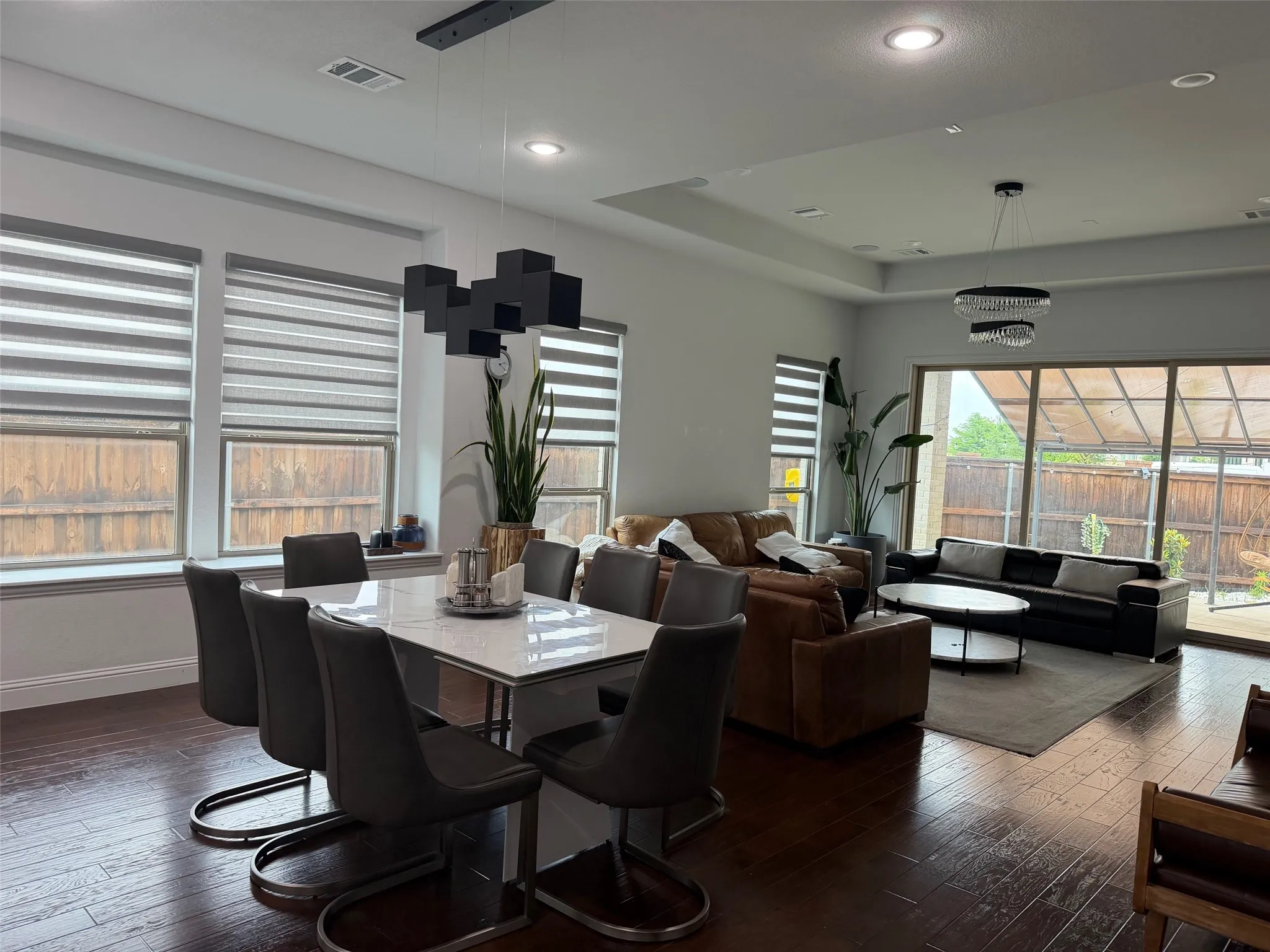 Open-concept interior featuring wood-finish flooring, tray ceilings, recessed lighting, geometric pendant fixtures, and large sliding glass doors