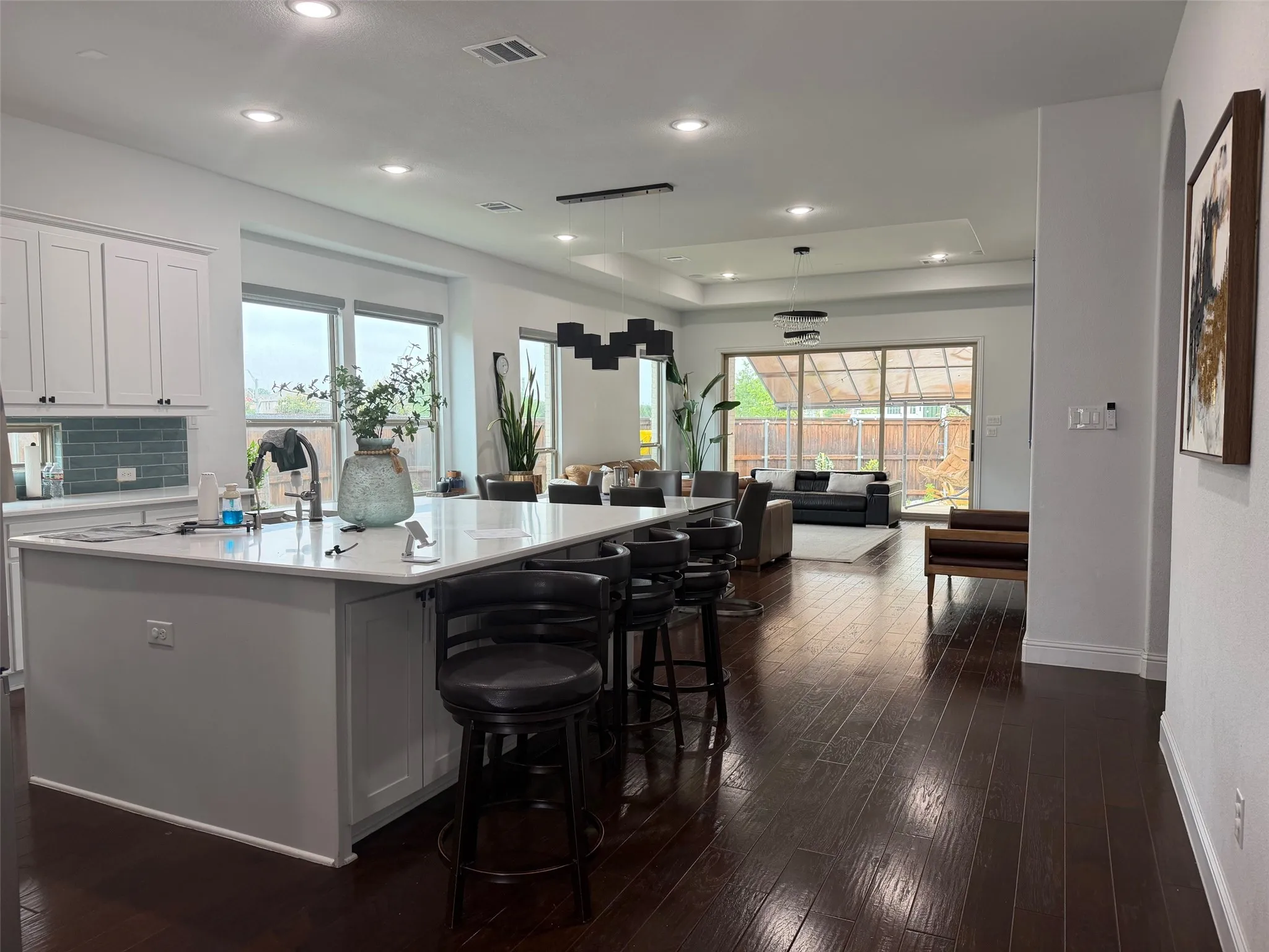 Kitchen featuring a spacious island with quartz countertops, custom white cabinetry, blue tile backsplash, wood-finish flooring, and recessed ceiling lighting