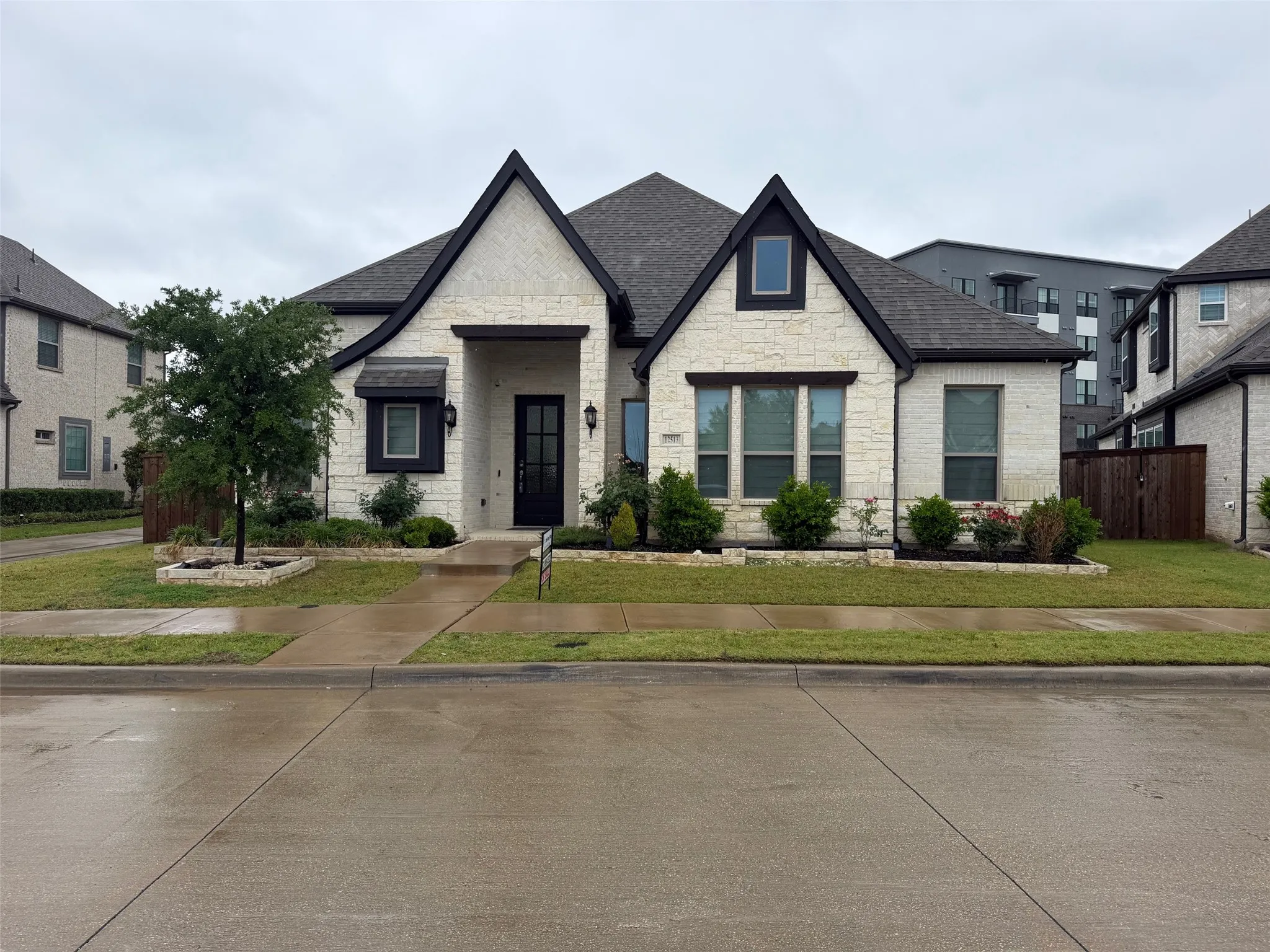 Multi-gabled exterior featuring light stone masonry, high-contrast dark window trim, a recessed entryway, and manicured landscaping