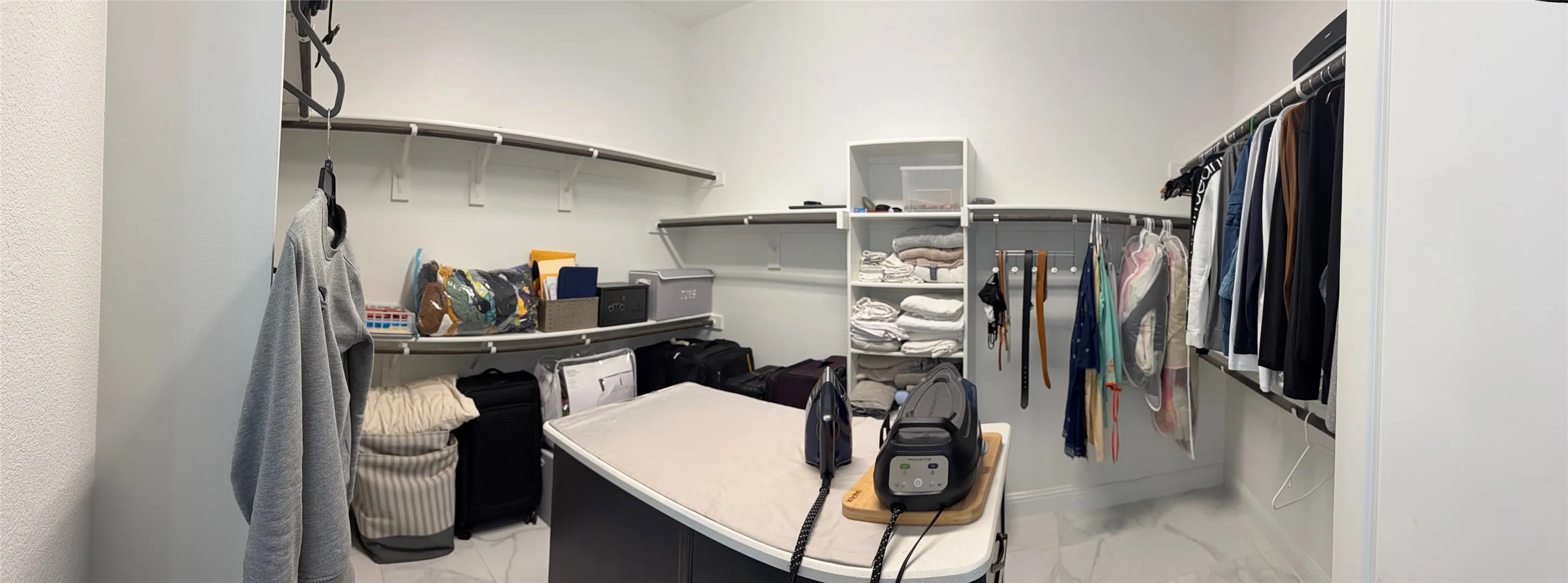 Walk-in closet featuring extensive built-in shelving, white tiered organization tower, multi-level clothing rods, and light-toned stone-patterned flooring