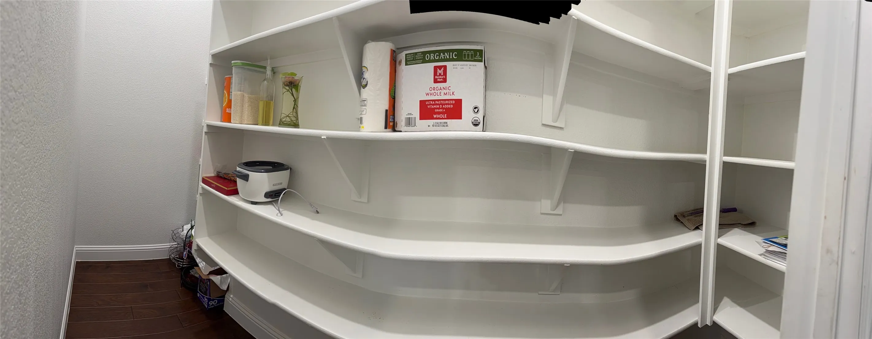 Storage pantry featuring white custom curved shelving and wood-finish flooring