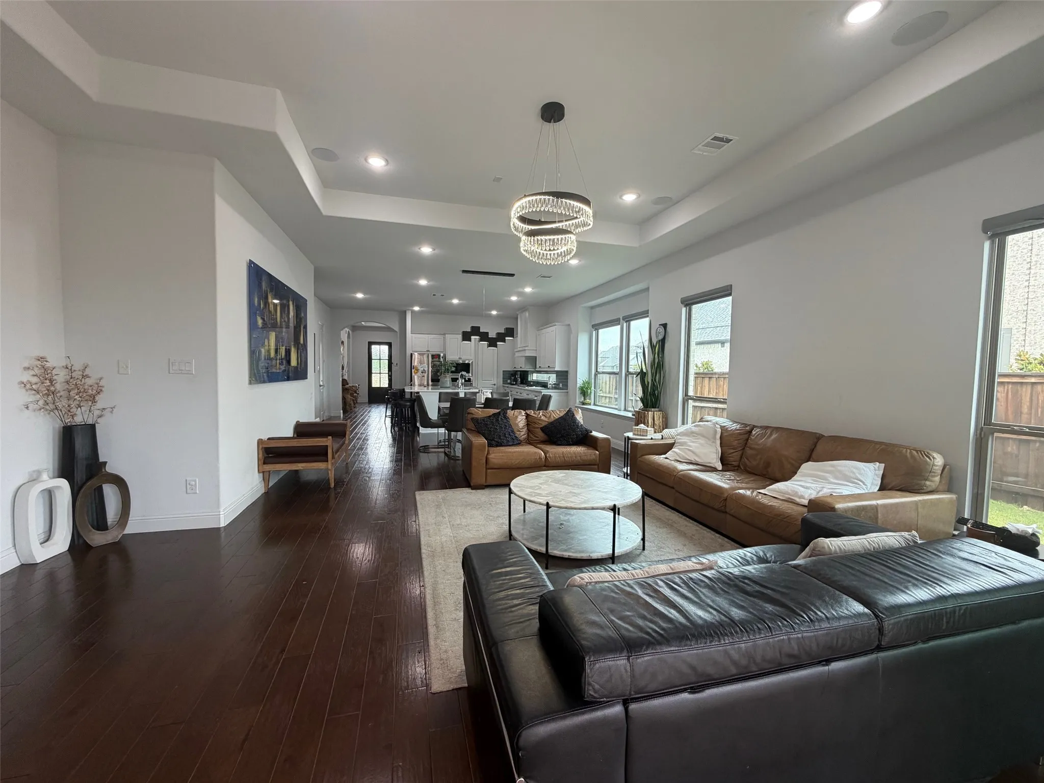 Open-concept interior featuring dark wood-finish flooring, recessed lighting, a tray ceiling, and a modern tiered chandelier