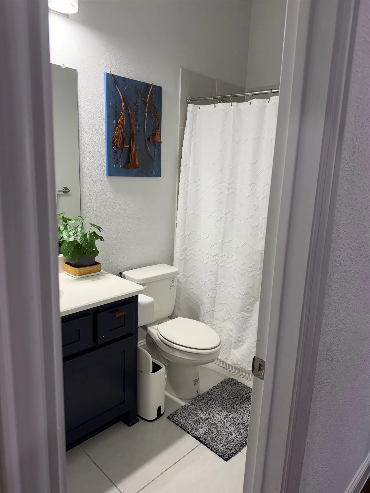 Dark-finish vanity cabinetry with a solid-surface countertop, rectangular wall-mounted mirror, and tile flooring