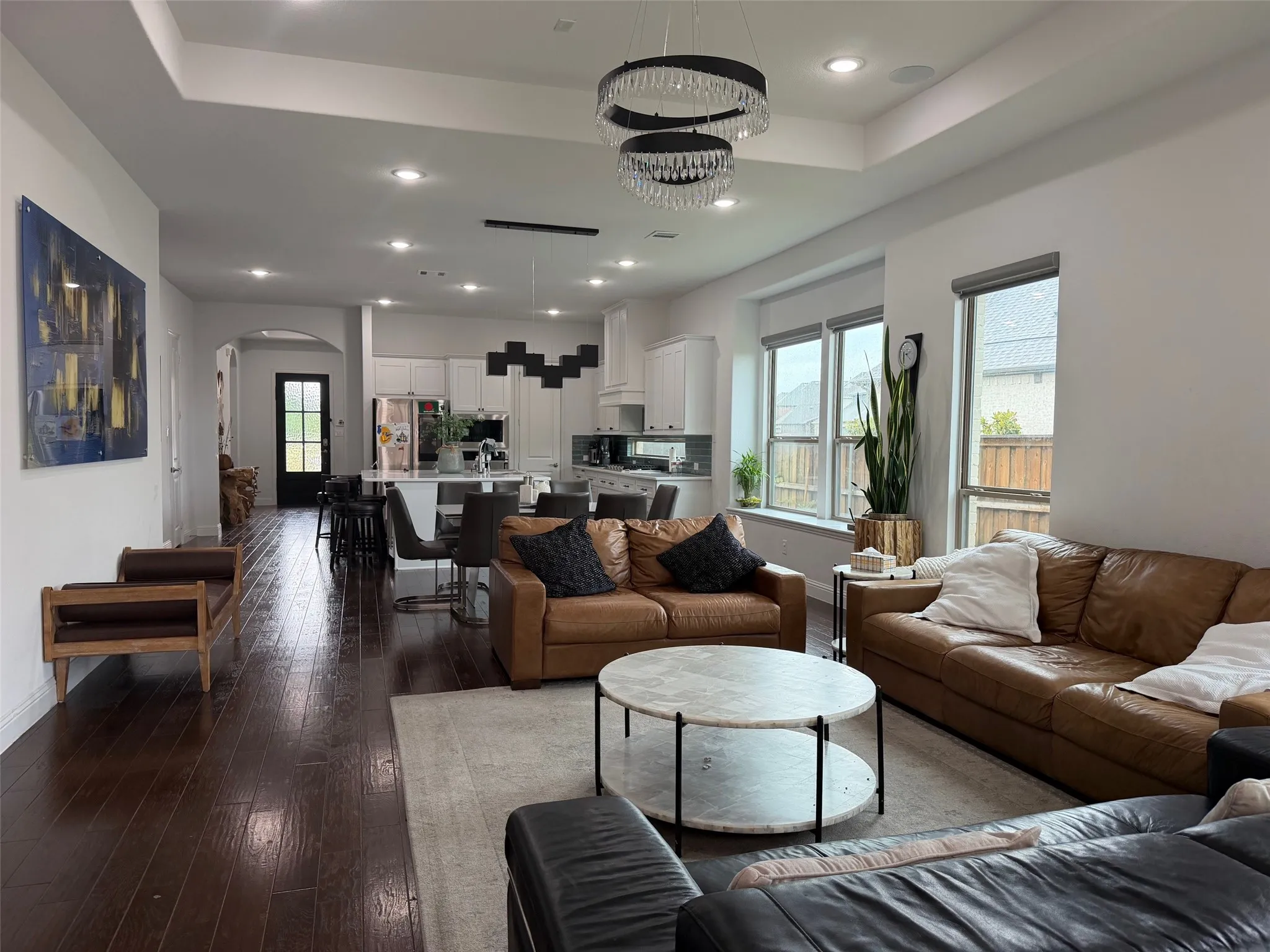 Open-concept living space featuring wood-finish flooring, tray ceilings, recessed lighting, and a tiered crystal chandelier