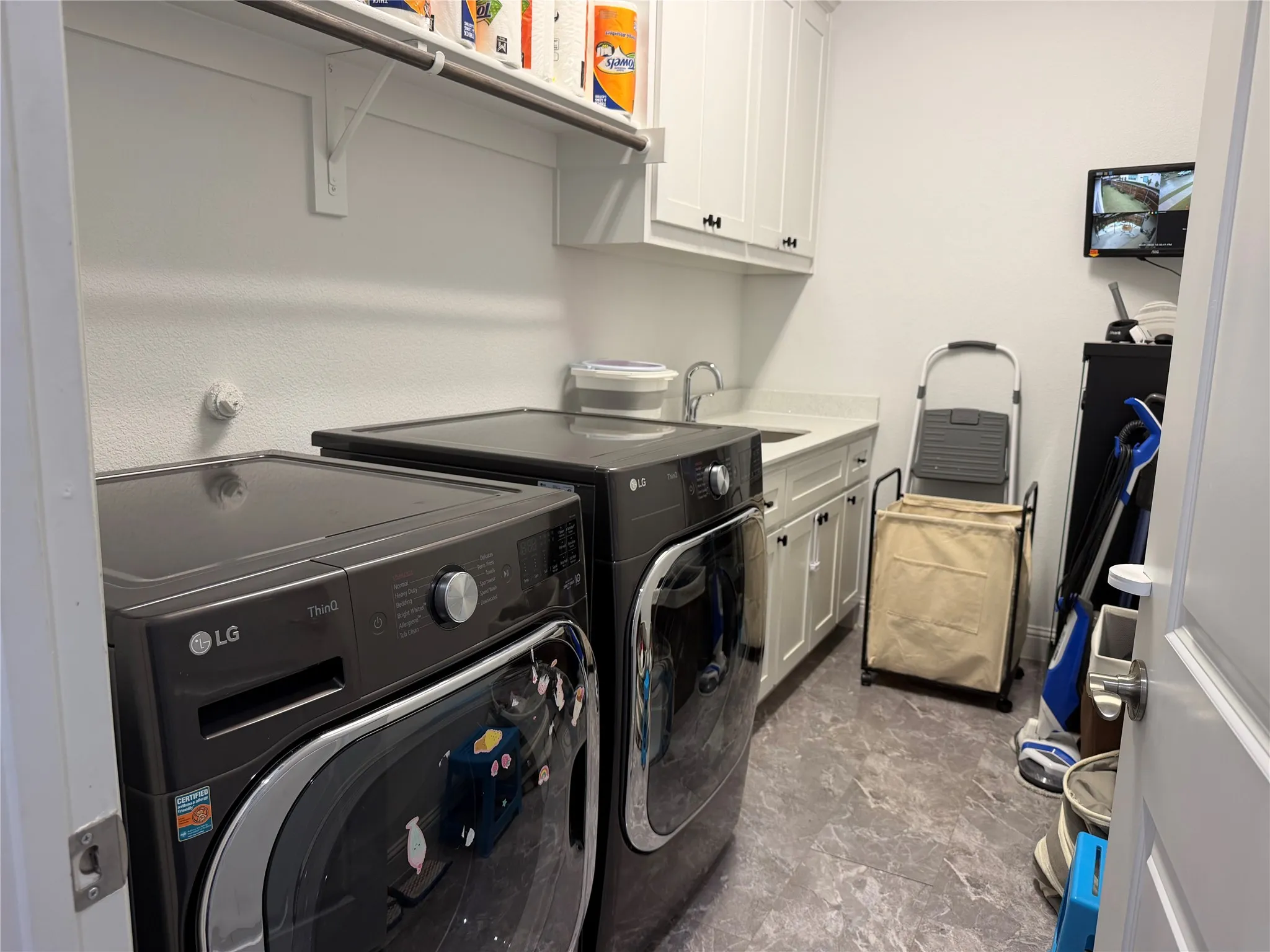 Laundry room featuring shaker-style white cabinetry, stone-finish countertops, integrated basin sink, overhead shelving, and tiled flooring