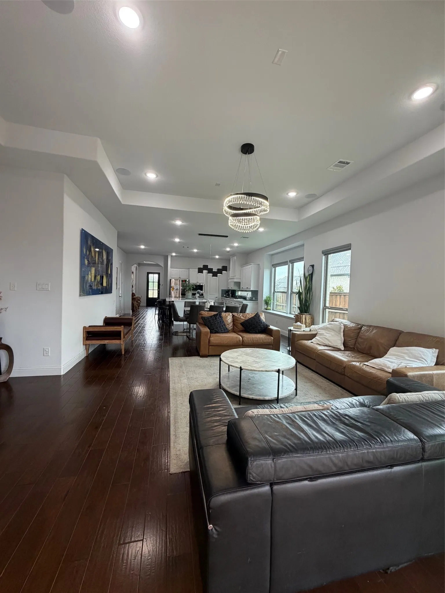 Open-concept living space featuring a tray ceiling, dark wood-finish flooring, recessed lighting, and a tiered modern chandelier
