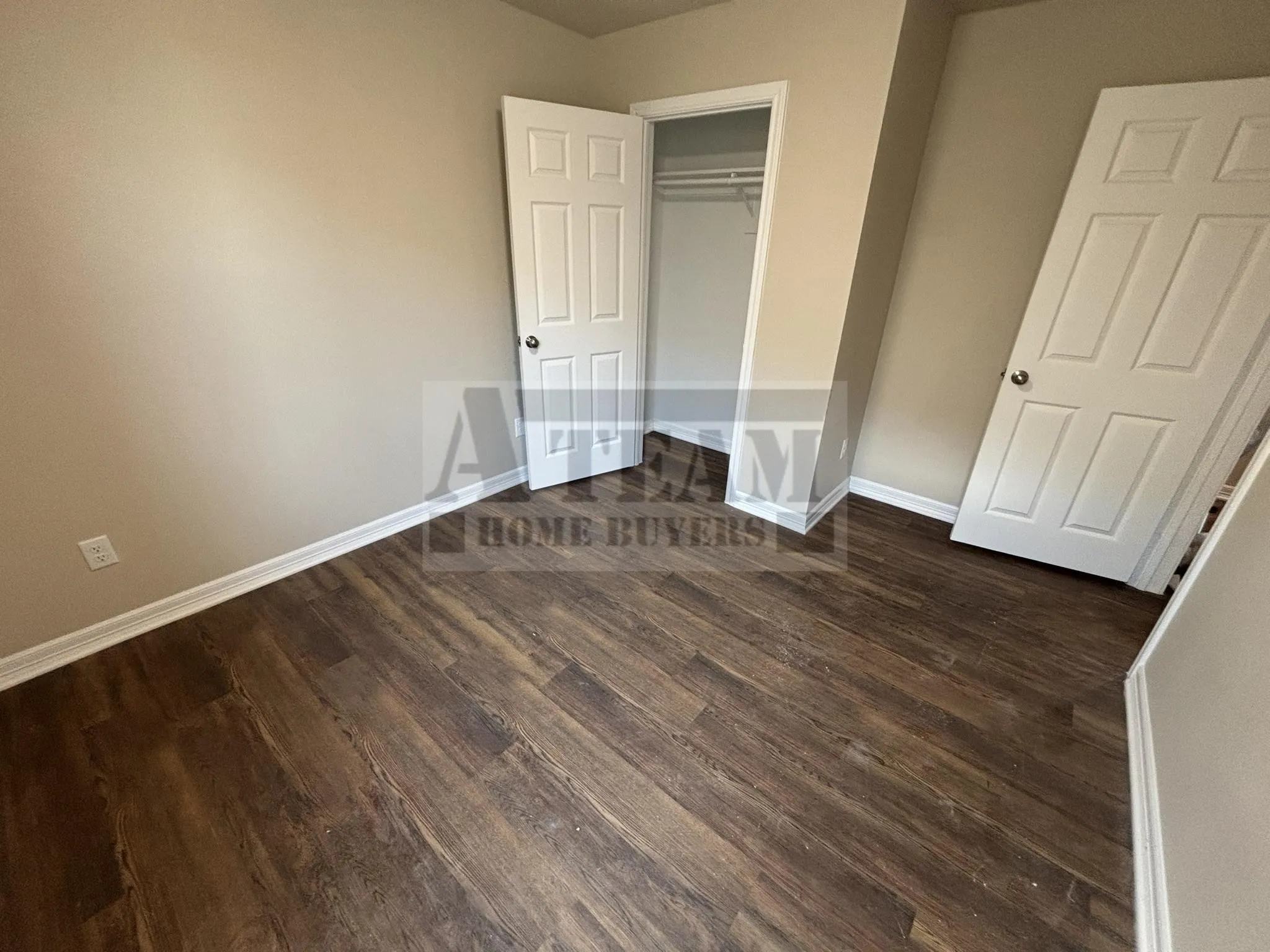 Room featuring wood-finish flooring, neutral wall paint, two white paneled doors, and a built-in reach-in closet with integrated shelving